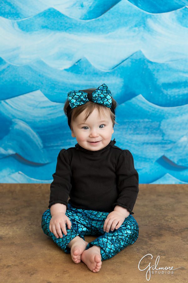 1 year old sitting in front of a blue water background