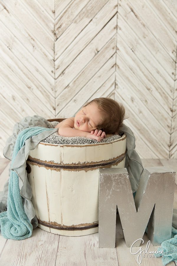 baby boy sleeps in a bucket next to a large letter M