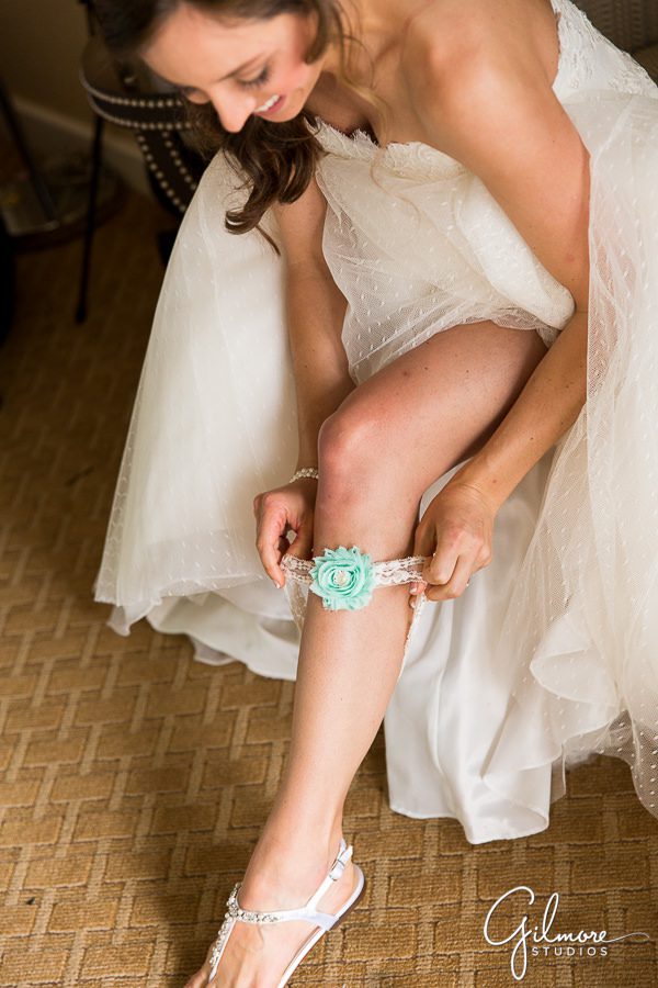 bride putting on the white and teal garter