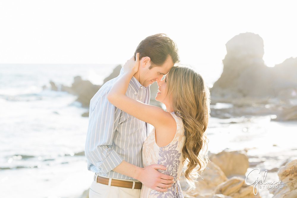 Newport Beach Engagement Session, romantic southern california lifestyle, engaged couple, kiss, outfits, portrait shoot locations, floral dress, rocks, ocean, waves, sunset, natural light