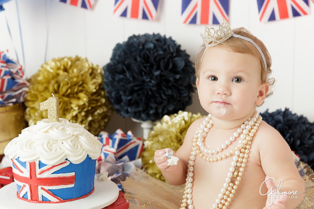 Princess London's 1st Birthday, closeup, cake smash, props, england theme, eating, pom poms, flags, outfit, skirt, tutu, headband, necklaces, one year old