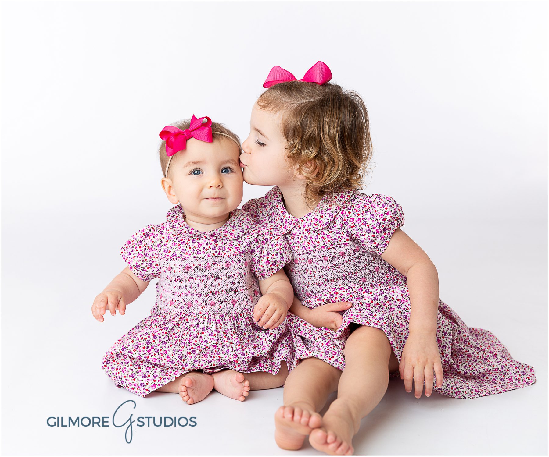 Newport Beach Children's Photography, baby sister, big sister, siblings, kids, light pink background, sitting up, 6th months old, 6th month session, baby girl, baby prop, pink bow, floral dress, six months old