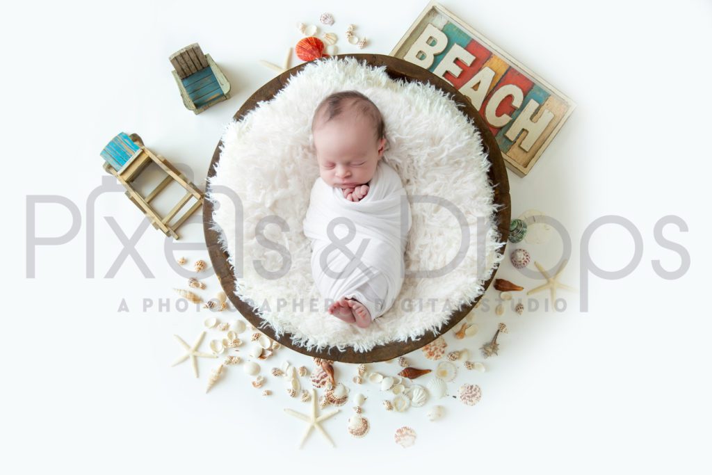Newborn Digital Backdrops styled by Pixels and Drops with a life is a beach attitude. With white photo for swaddling the newborn baby. Multiple seashells starfish and colorful beach sign complement the dark brown bowl