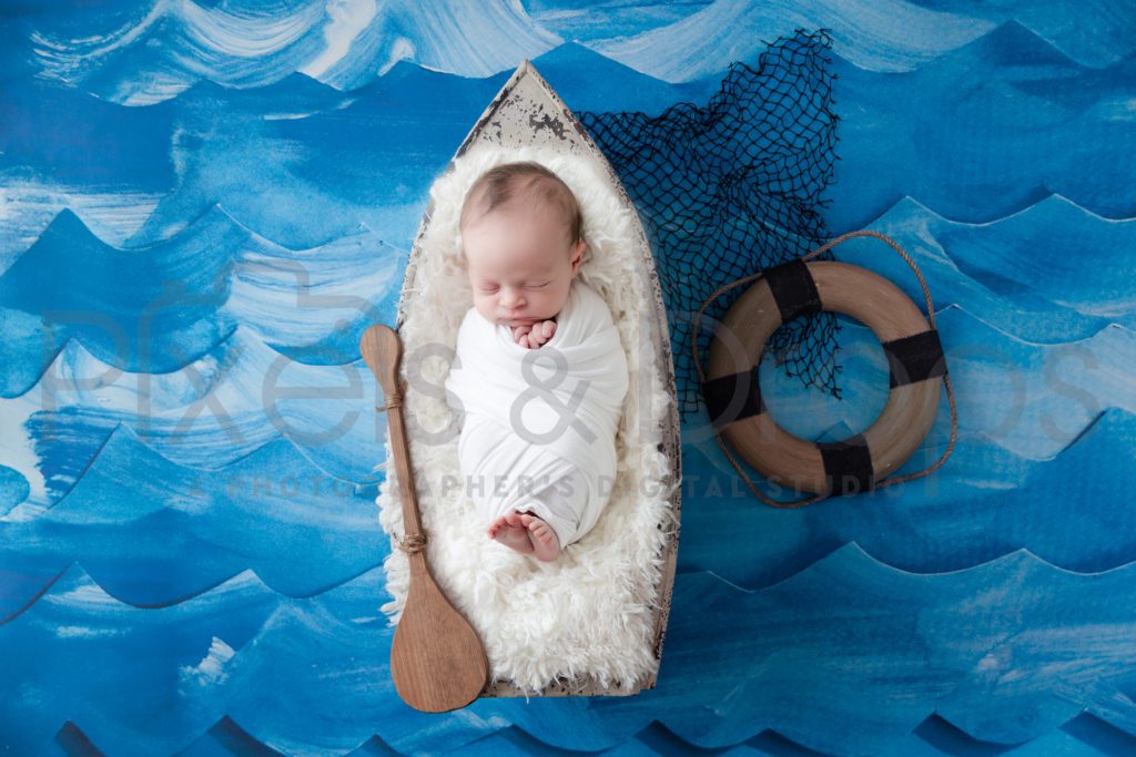 Newborn Digital Backdrops styled by Pixels and Drops with multiple shades of blue create an ocean effect as the background. Black fishing net along with a white sailboat and Orr. The life preserver is a great touch to the ships ahoy