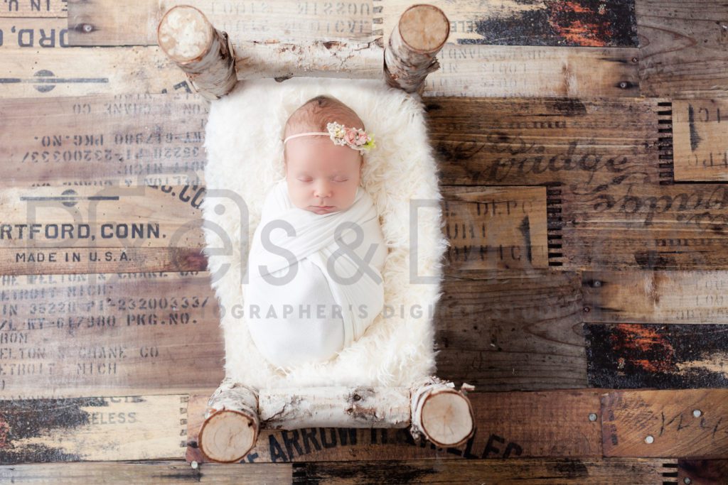 Newborn Digital Backdrops styled by Pixels and Drops with brown plank flooring and complimentary wooden bed. Custom handmade bed with a white faux fur blanket to rest on top of the bed
