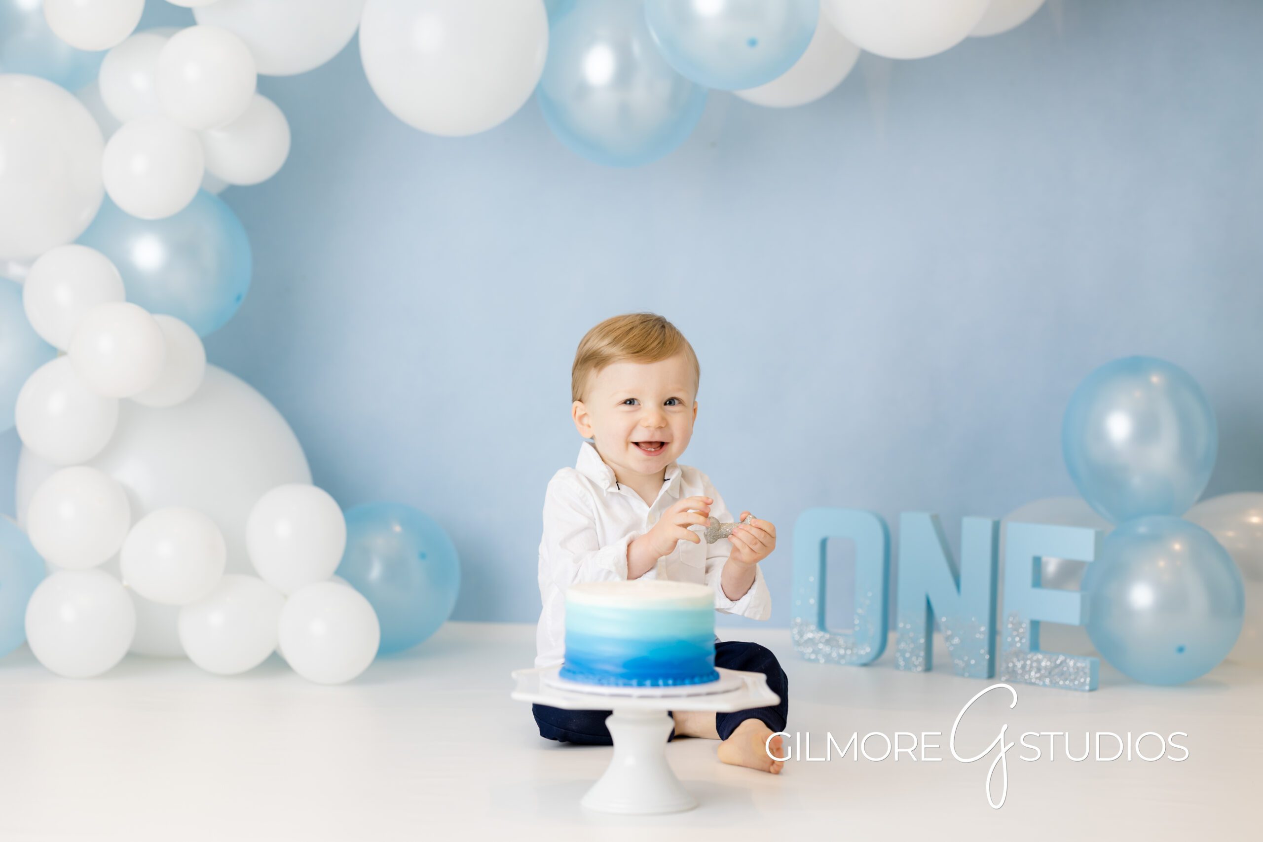 Simple 1st Birthday Cake Smash - Gilbert, AZ Photographer, baby on blue and white balloon background, brother, first birthday, cake smash photo shoot, Gilmore Studios
