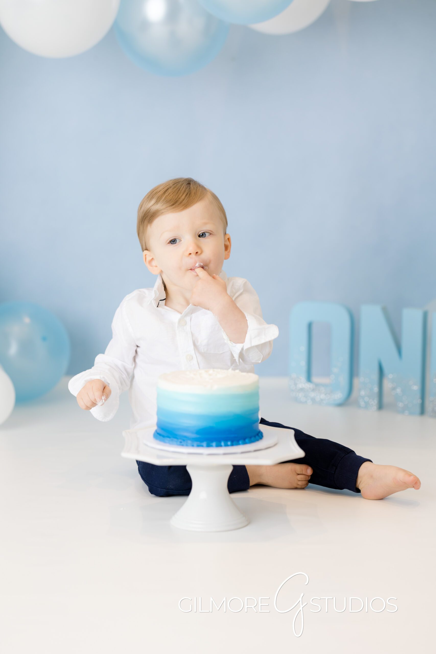 Simple 1st Birthday Cake Smash - Gilbert, AZ Photographer, baby on blue and white balloon background, brother, first birthday, cake smash photo shoot, Gilmore Studios, blue and white cake