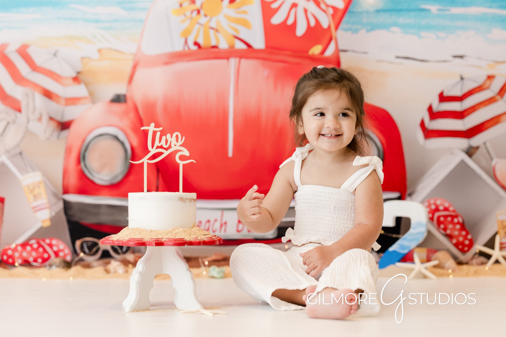 Summer Cake Smash VW Bug Beetle Newport Beach, beach, yellow polka dot bikini, gilmore studios, cake smash, little girl 2nd birthday, happy bday, child photography, vw beetle, vw bug, volkswagon, red and white, beach, waves, sand, white cake, vanilla frosting, buttercream, excited, ponytail, white romper, surfboards, yellow and red