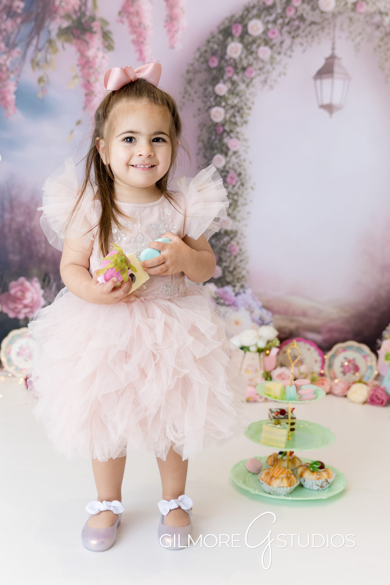 tea party cake smash, little girl smiling, pink dress, pink bow, tea party treats, little girl holding treats, gilmore studios