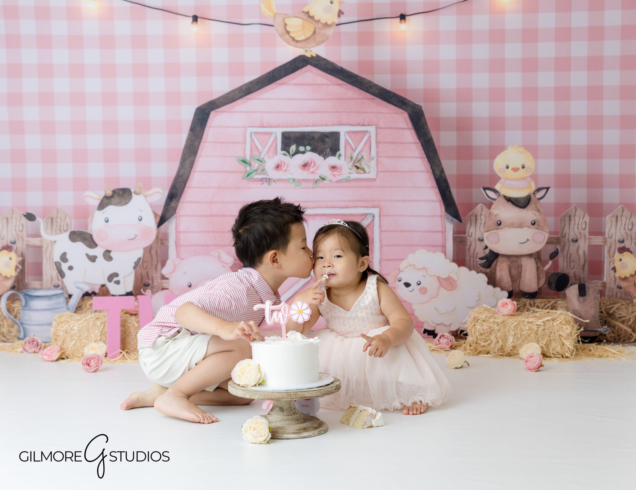 Cake smash portrait session for 2-year-old with farm theme, Pastel pink farm photography backdrop for toddler birthday,Newport Beach child portrait with pink barn backdrop and cake
