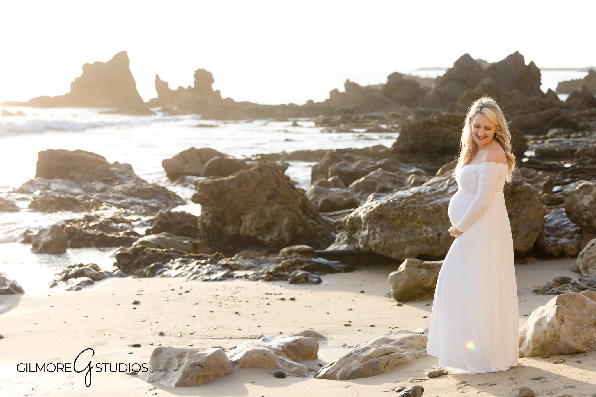 Expecting mom posing in flowy dress at Corona del Mar beach, Sunset maternity photography by professional photographer in Newport Beach