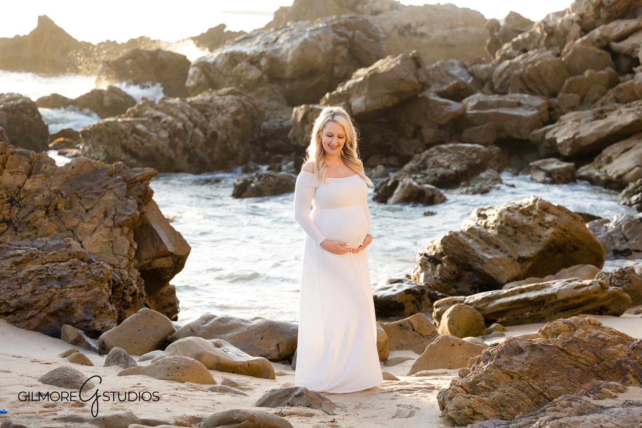 Little Corona beach maternity shoot with natural cliffs, Pregnancy portrait with ocean backdrop by Gilmore Studios