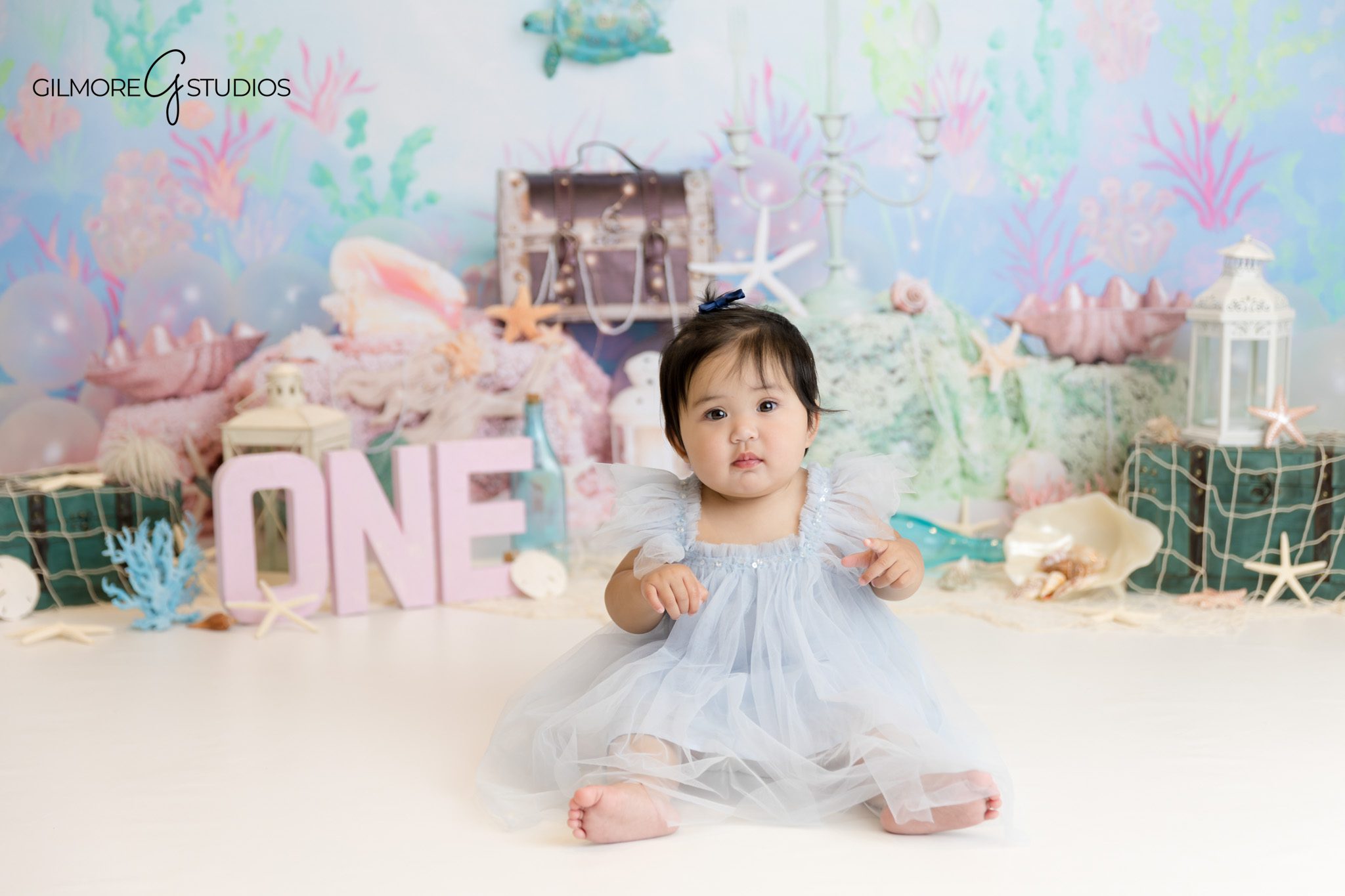 Mermaid-themed cake smash photographed with seashell and pearl decor.

One year photoshoot photographer capturing baby girl smiling in mermaid outfit.