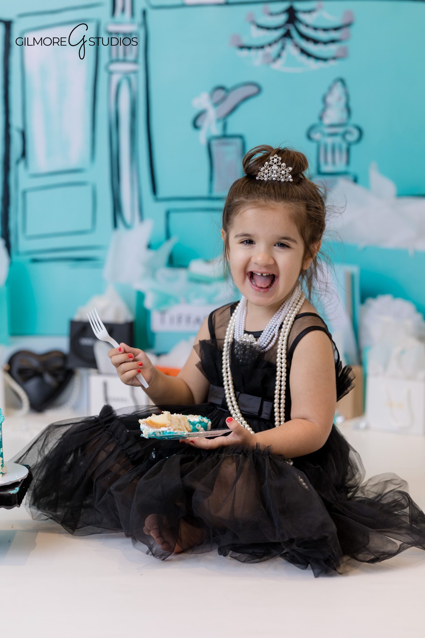 Photographer capturing Tiffany styled birthday backdrop with gift boxes.
Tiffany theme 3rd birthday portrait with white balloons and teal styling.