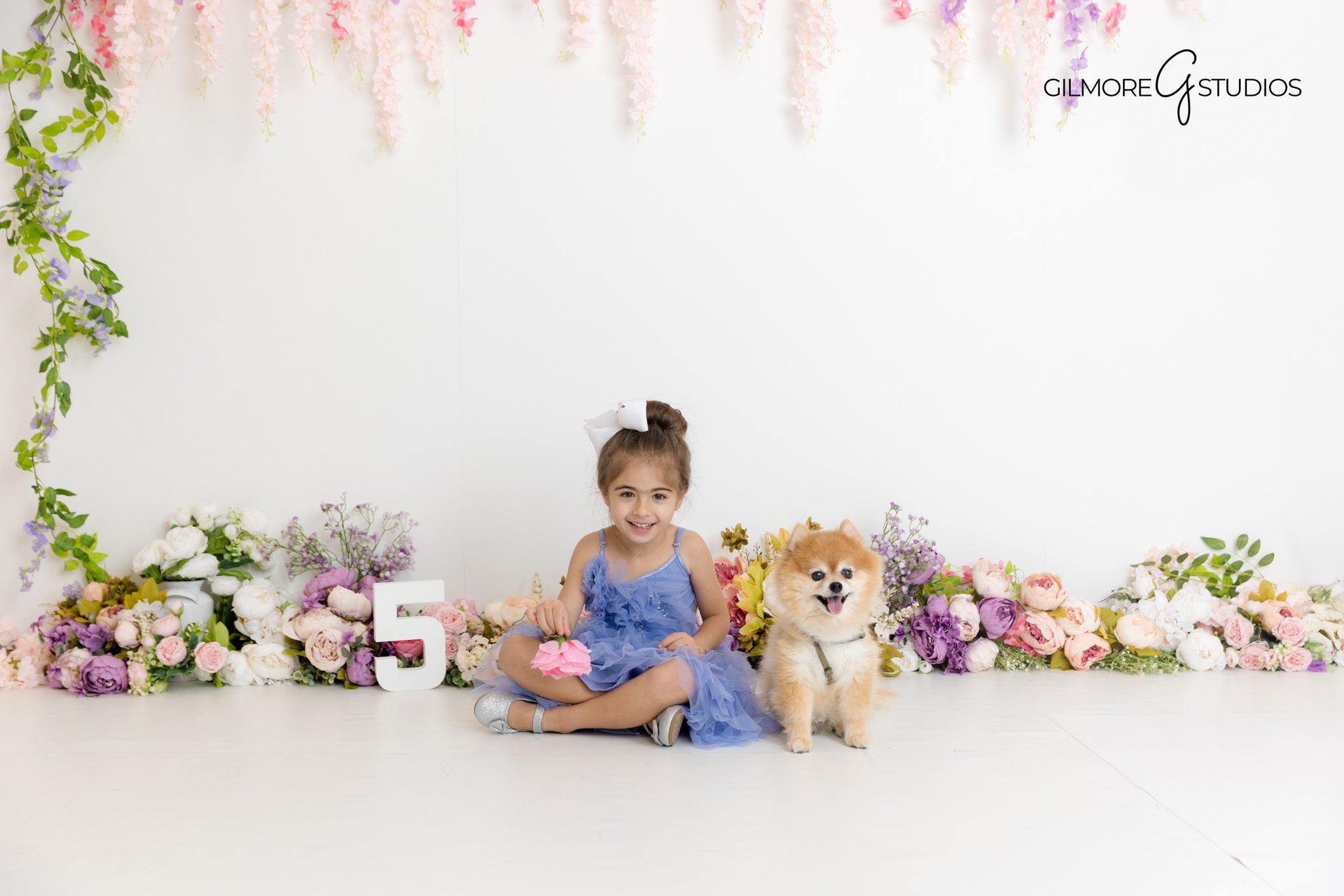 5-year-old girl in a pink dress sitting in front of a floral backdrop during a studio birthday photo session in Gilbert, AZ