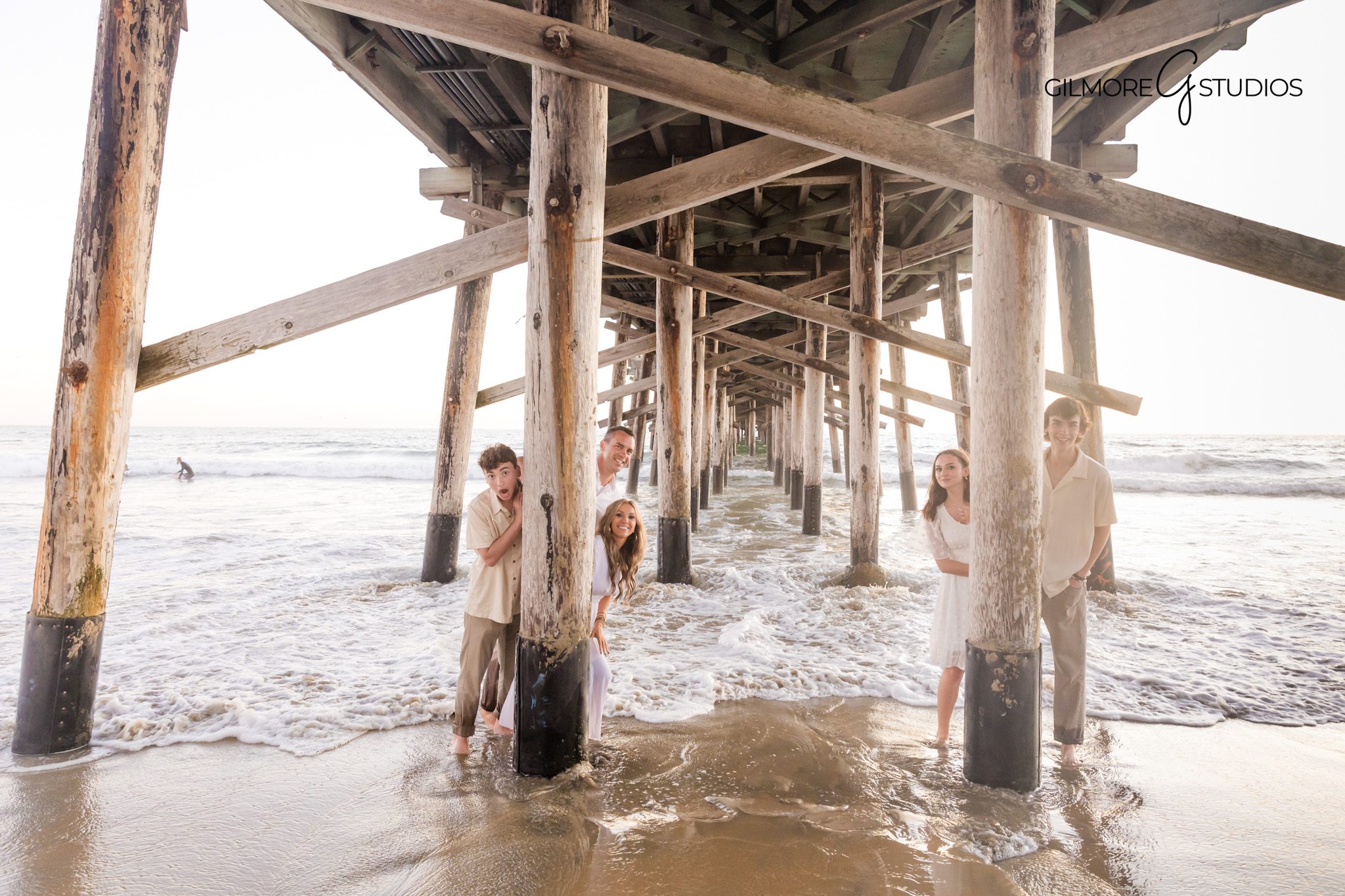 Beach photographer capturing warm sunset glow on family portraits.
Newport Beach Pier family photography with ocean waves behind them.
