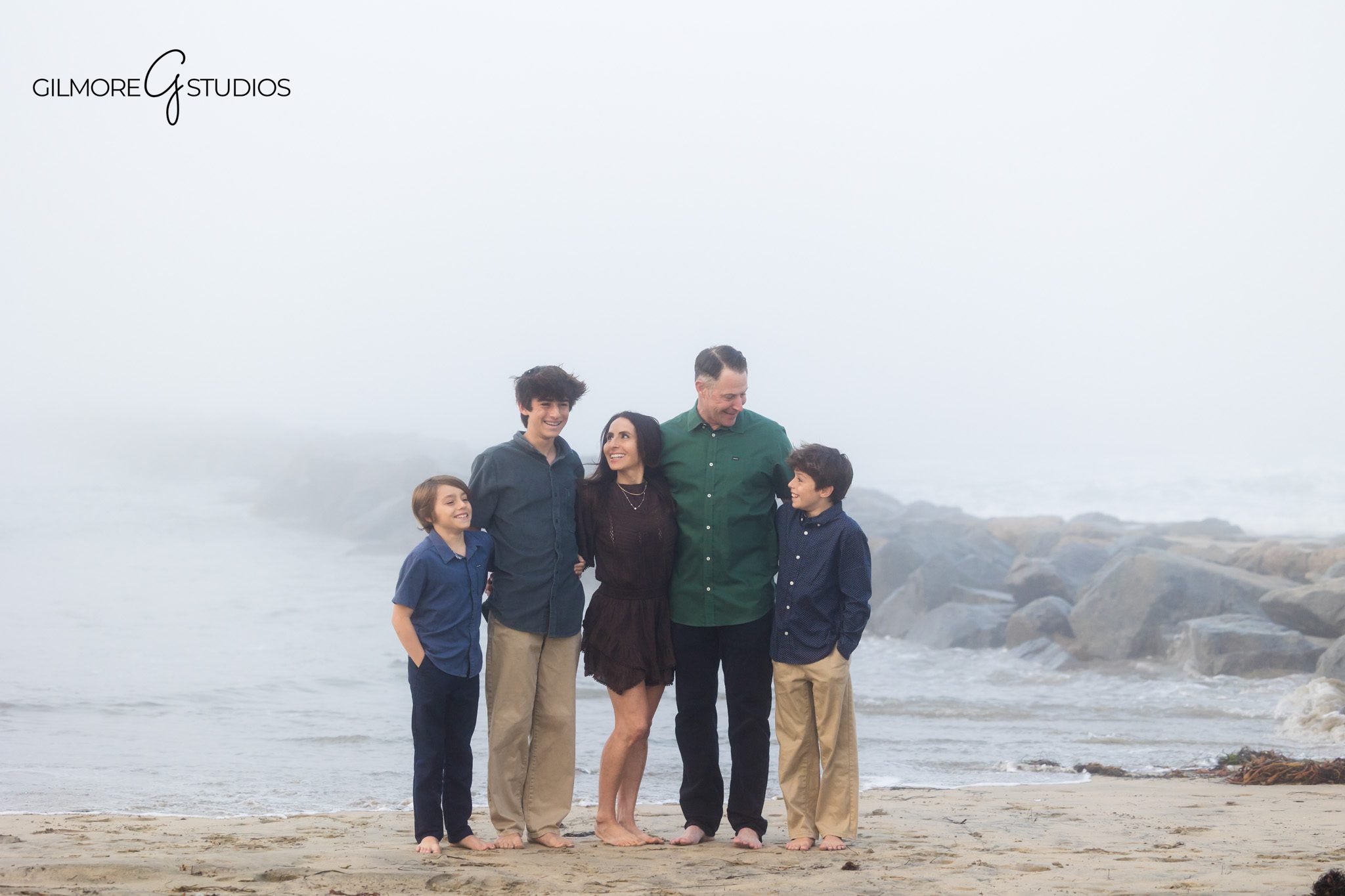 Photographer documenting parents and kids during foggy beach session.

Fog-softened family portraits by Orange County family photographer.