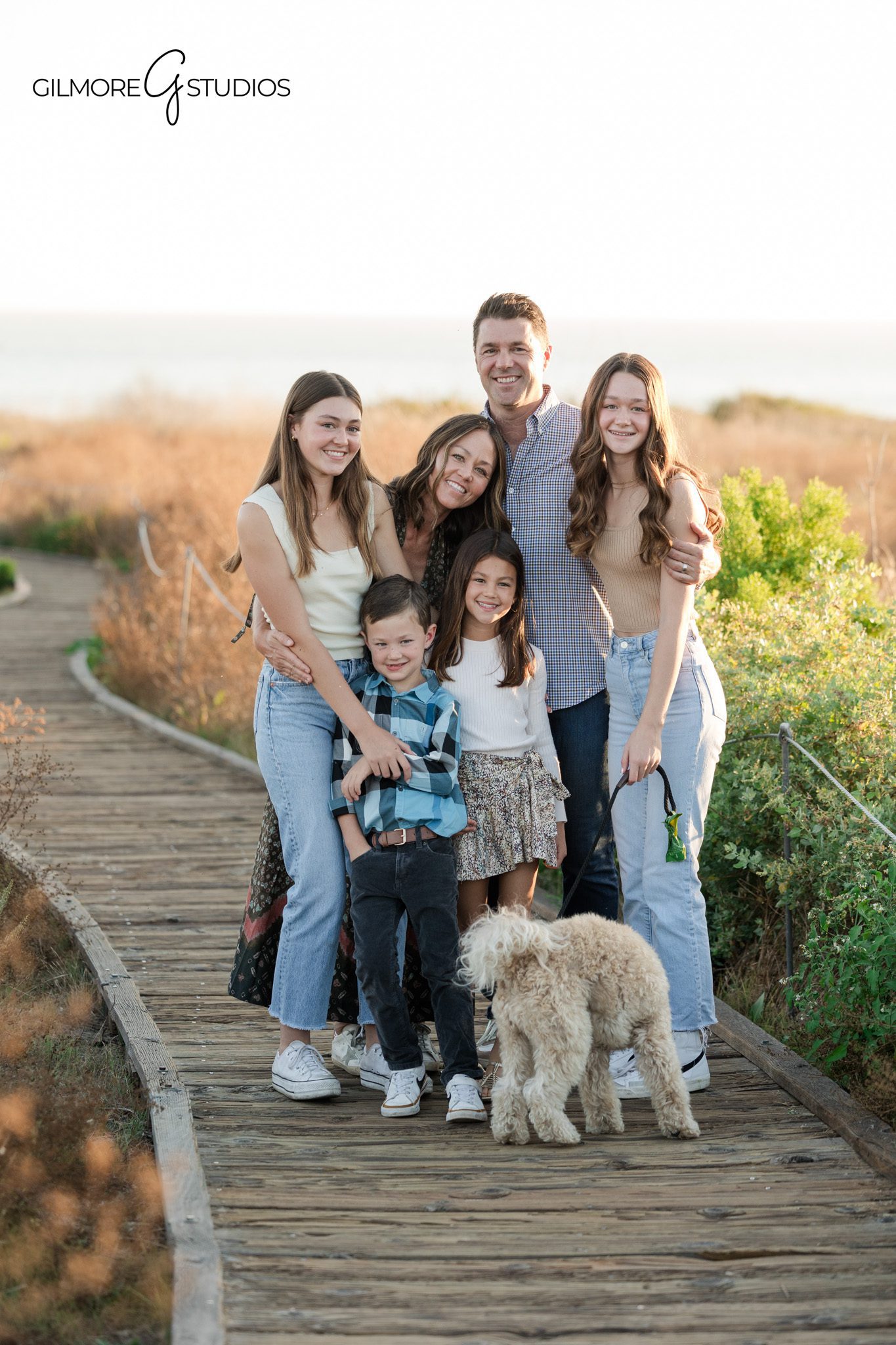 newport beach family photographer capturing kids laughing on boardwalk
family portrait crystal cove california with ocean and field background