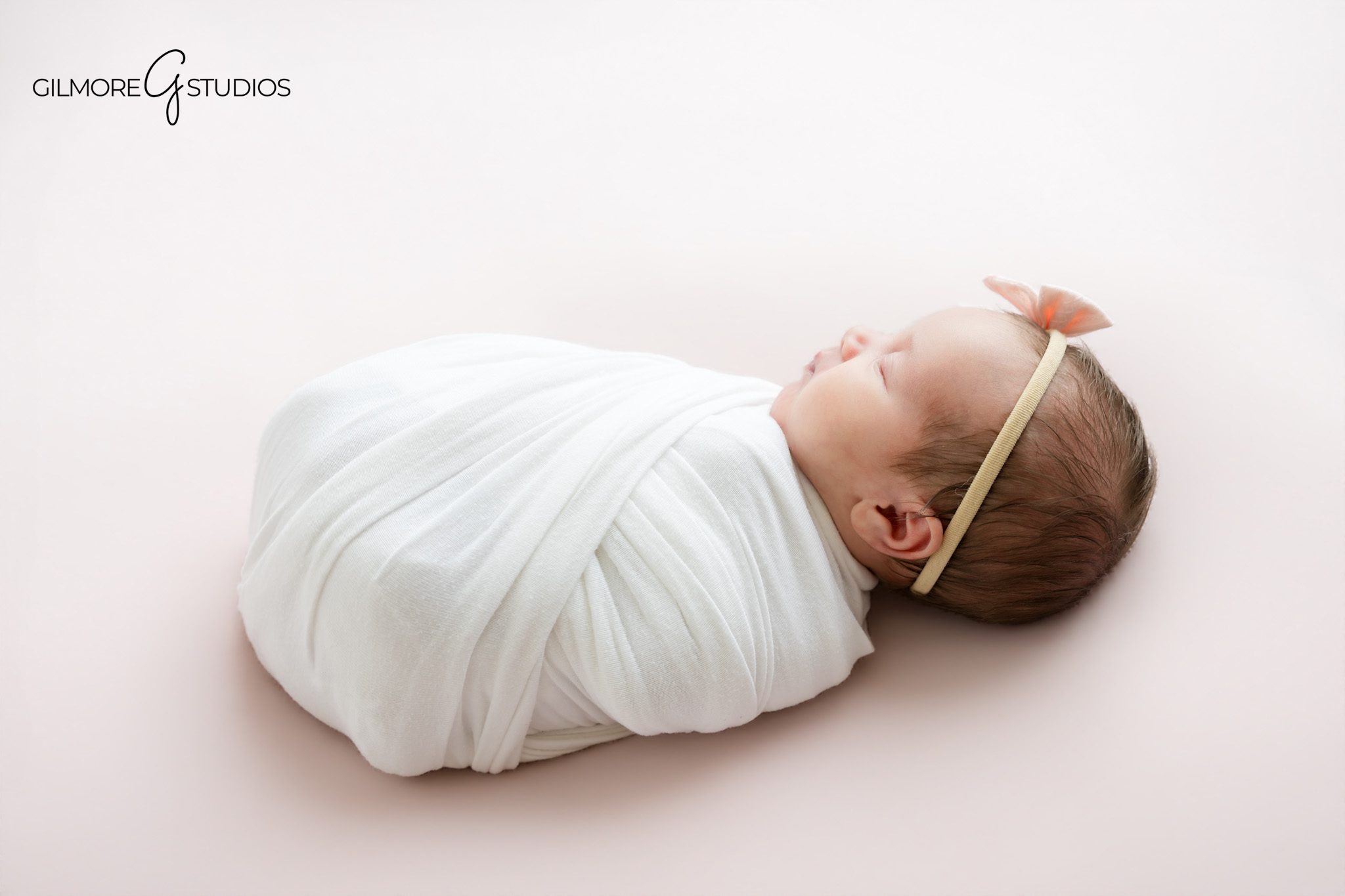 Gilbert Arizona newborn studio portrait of sleeping baby girl wrapped in white swaddle with blush bow