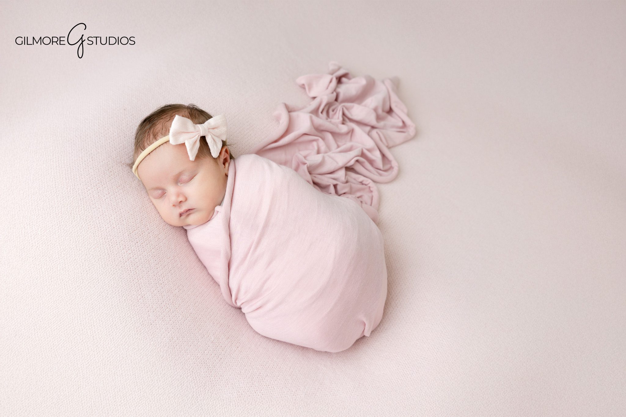 Baby girl newborn portrait session in neutral studio setup with soft white swaddle and floral headband