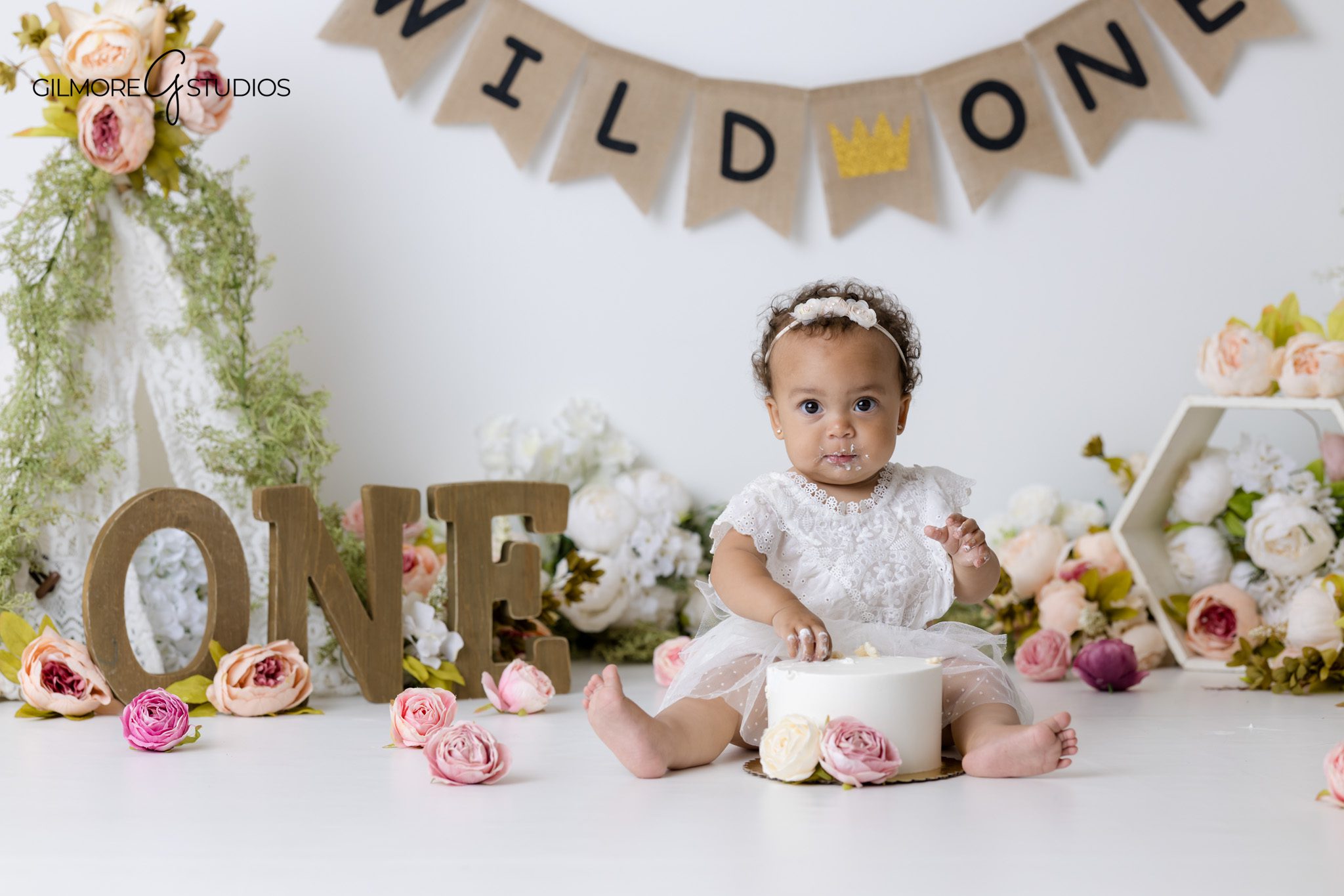 One year old photography Gilbert AZ featuring baby girl sitting beside floral birthday cake