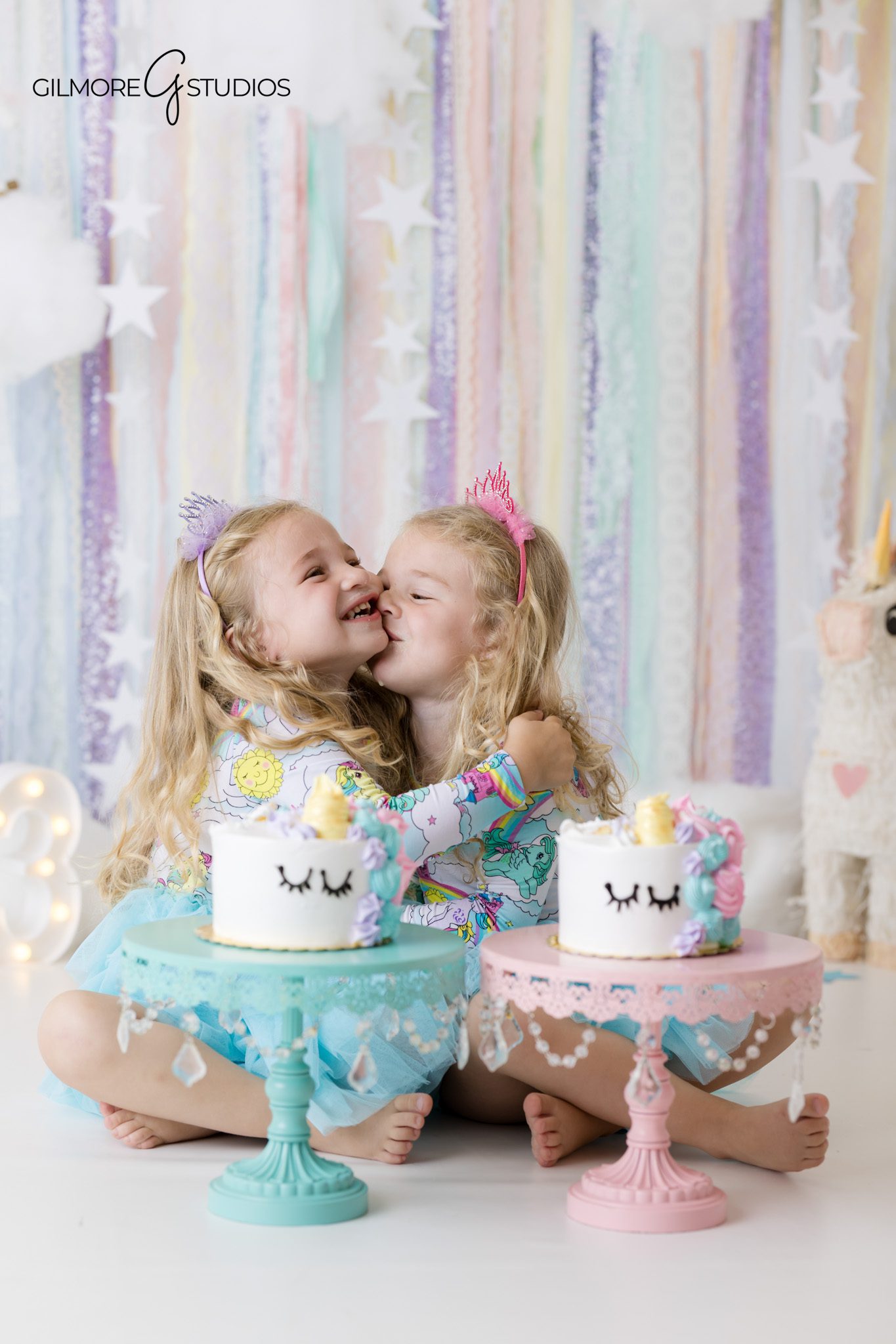 Twin girls sitting with unicorn cakes during a birthday photoshoot in Newport Beach
Unicorn cake smash session for twins with pastel balloons and clouds
Twin birthday photoshoot with pastel unicorn theme at Gilmore Studios