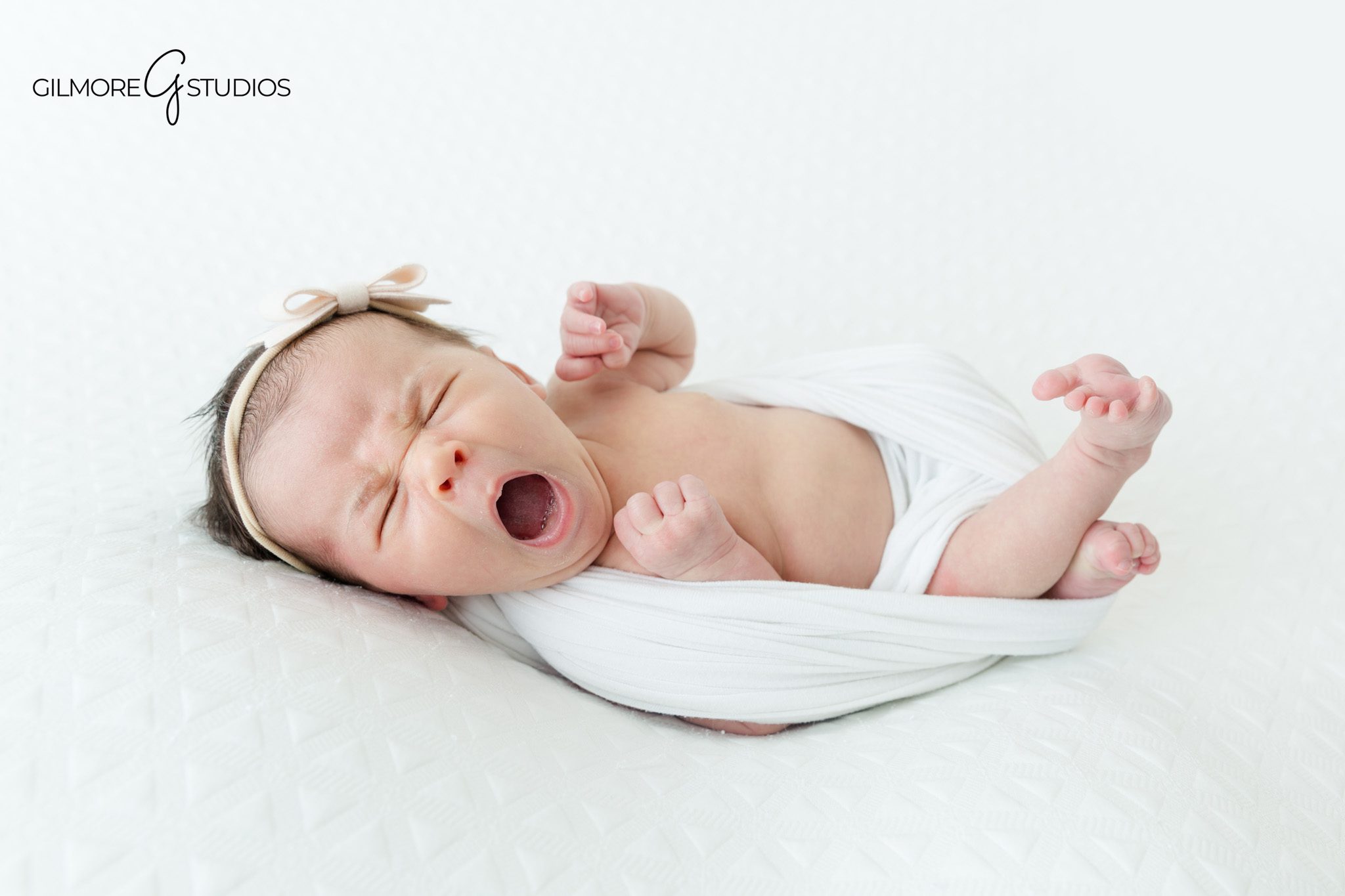 Newborn baby girl posed in a basket with white fur
Baby girl wrapped in cream during a newborn photography session