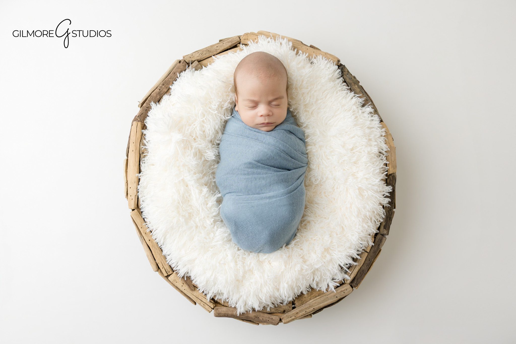 Newborn twins in mint and white wraps during Gilbert studio session
Baby boy twin wrapped in soft blue inside rustic basket