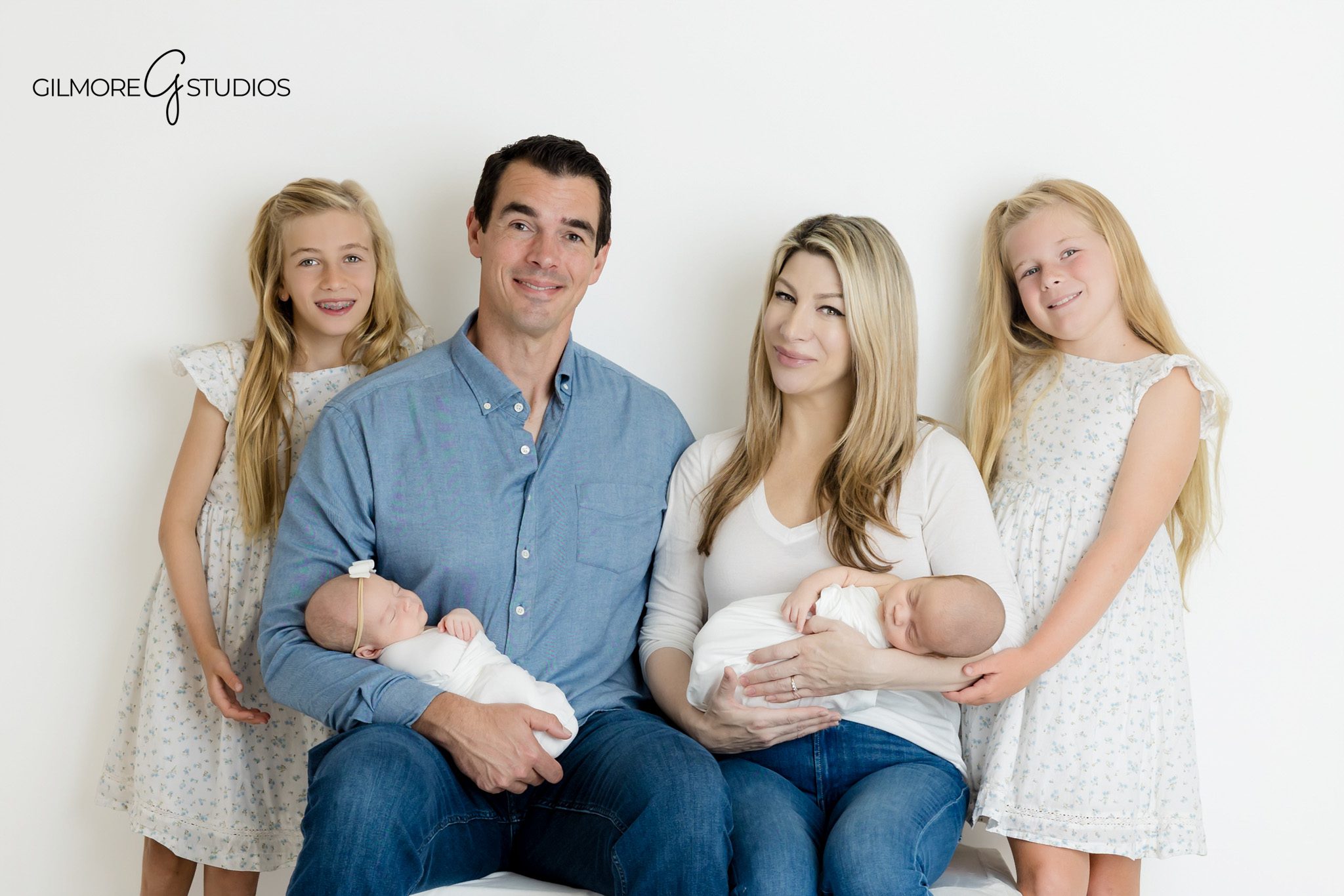 Gilbert newborn photographer capturing family with twin babies
Parents holding newborn twins with older daughters in studio