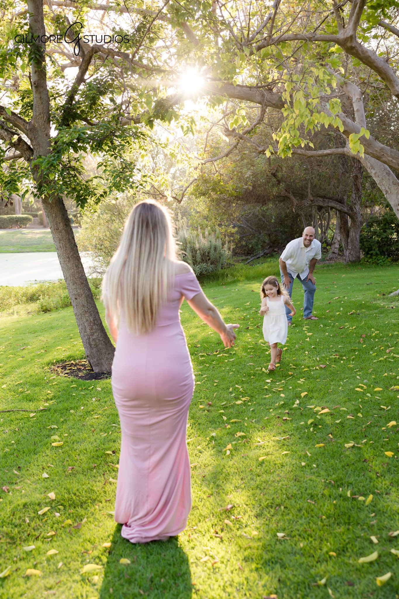 Toddler holding parents’ hands during maternity portrait session
Golden hour maternity photos with family in grassy park setting