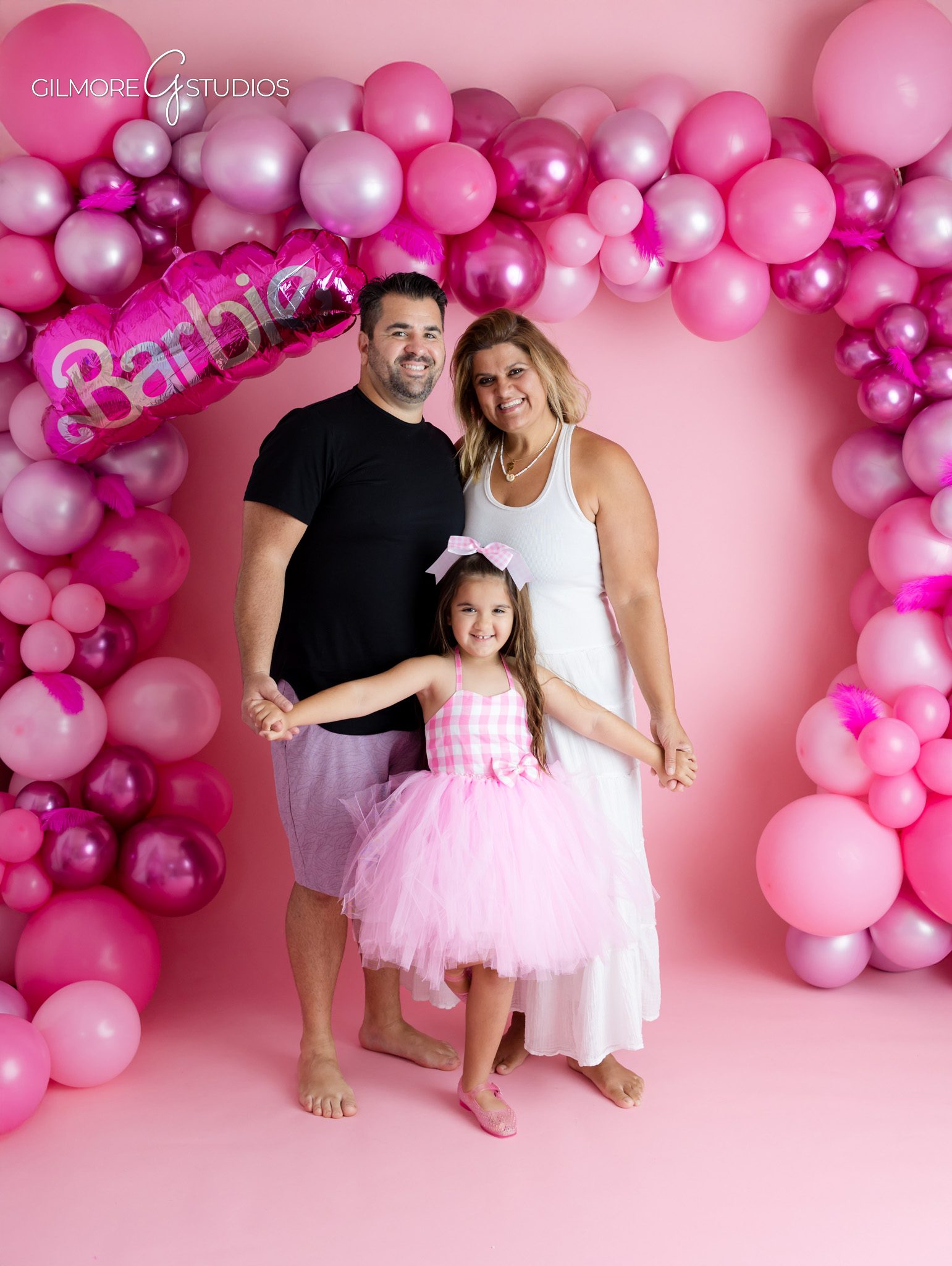 Little girl seated beside Barbie themed birthday cake
Pink Barbie birthday setup with cake, flowers, and number five