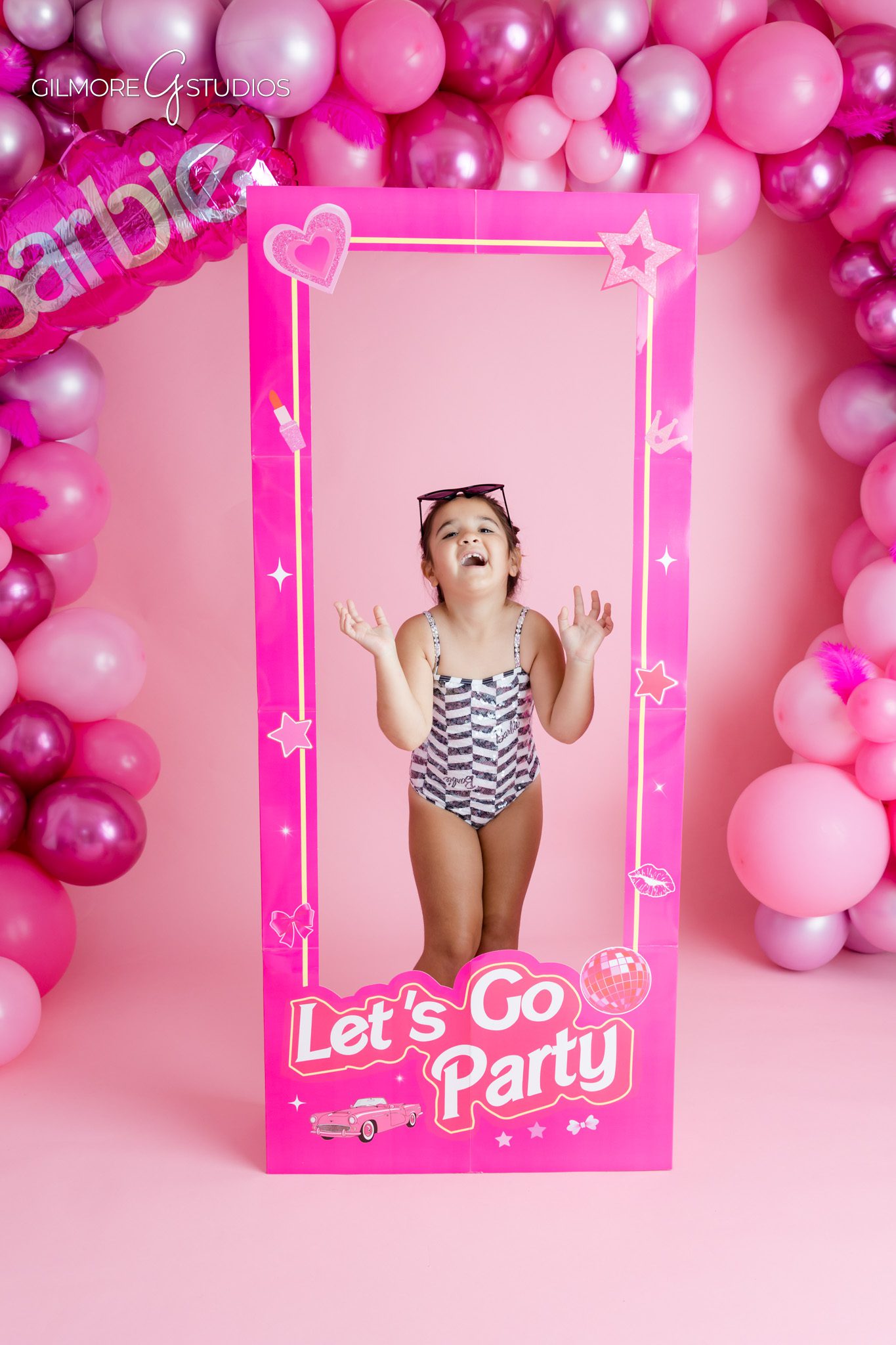 Pink birthday portrait session with Barbie sign and cake details
Little girl walking toward pink Barbie boutique backdrop