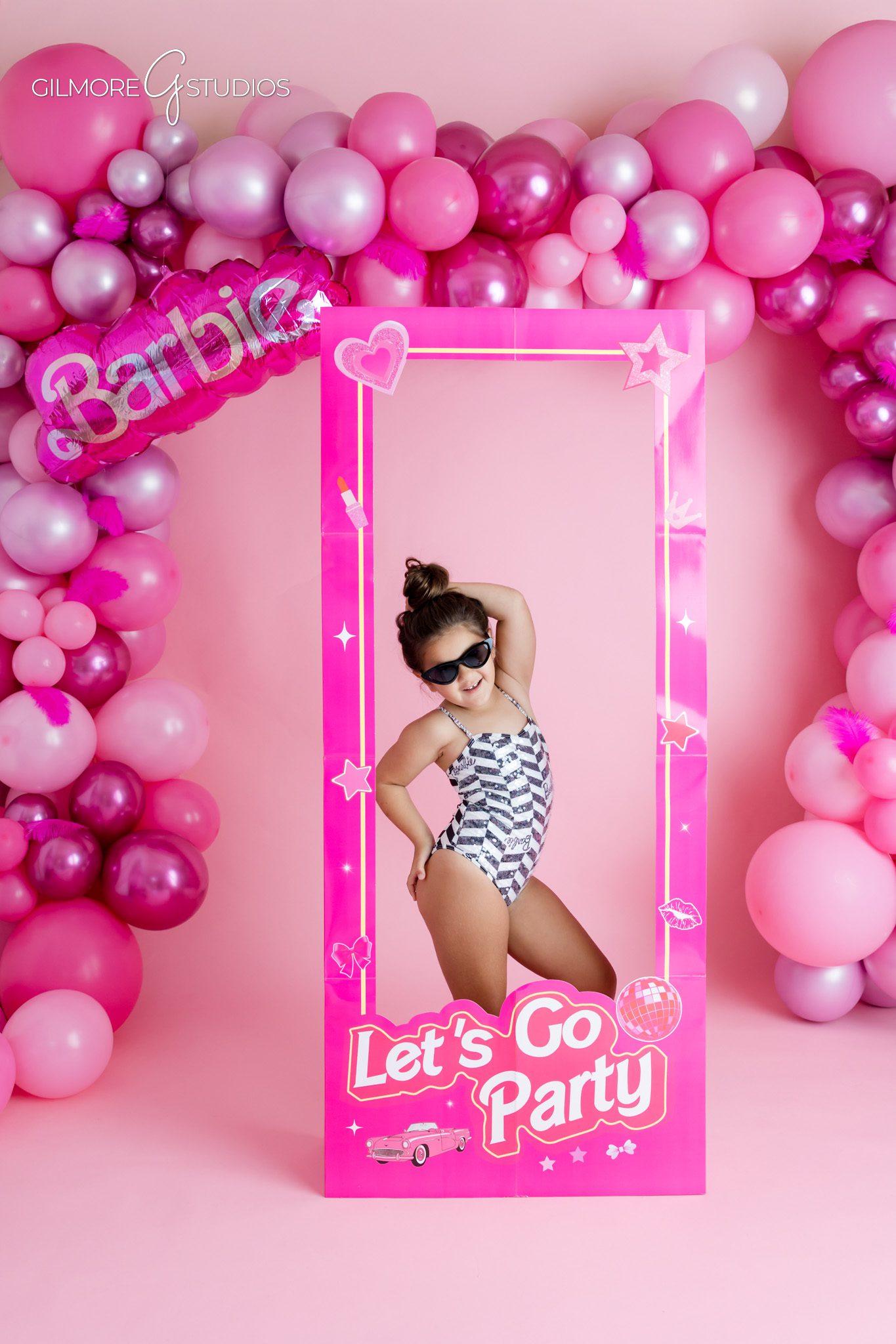 Barbie birthday photoshoot with pink balloons and party frame
Little girl posing inside pink Barbie party frame for 5th birthday photos