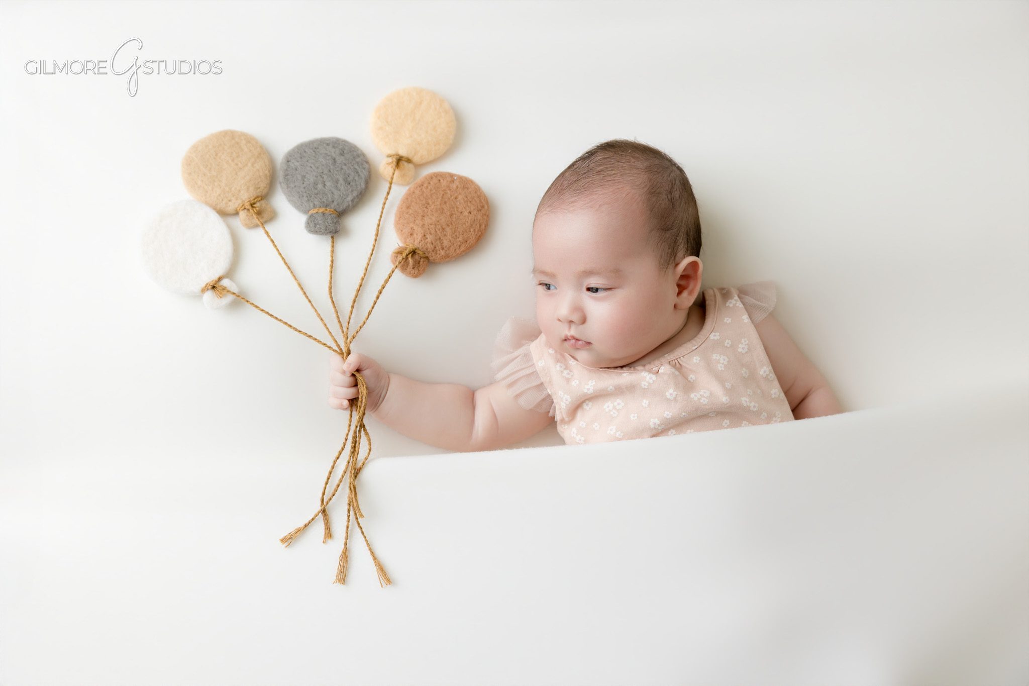 Baby girl photographed with soft felt balloon props in studio
Older newborn baby portrait with playful balloon styling