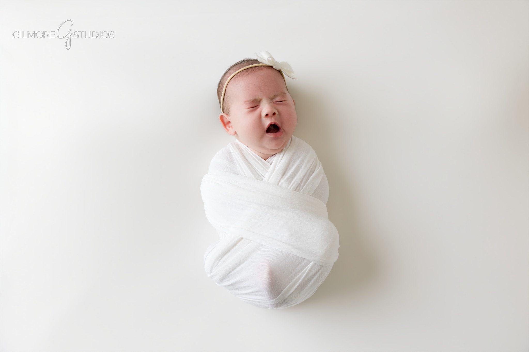 Baby girl awake in basket during older newborn session
Soft pink wrapped baby portrait on white studio backdrop