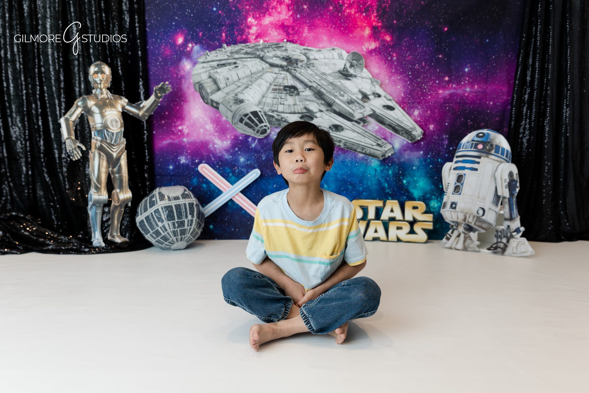 Boy sitting cross legged during space birthday session
Kids birthday photography with galaxy backdrop and robot props