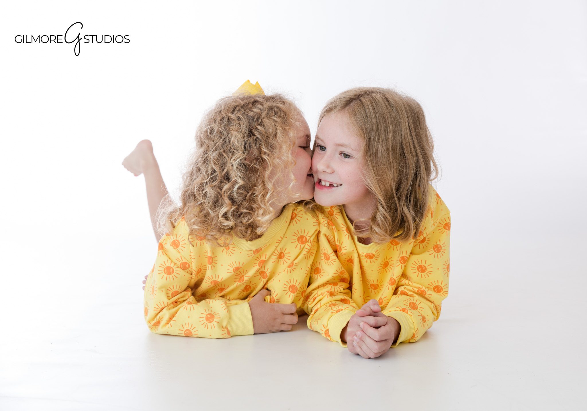 Sweet sibling pose with sisters facing each other in studio
White studio portrait of sisters holding hands