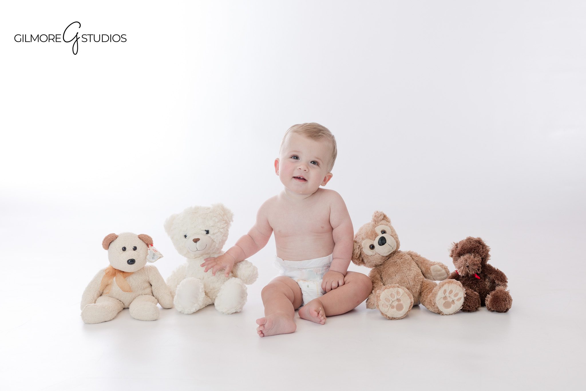 First birthday portrait with stuffed bears and soft studio styling
Baby boy smiling beside teddy bears before cake smash photos