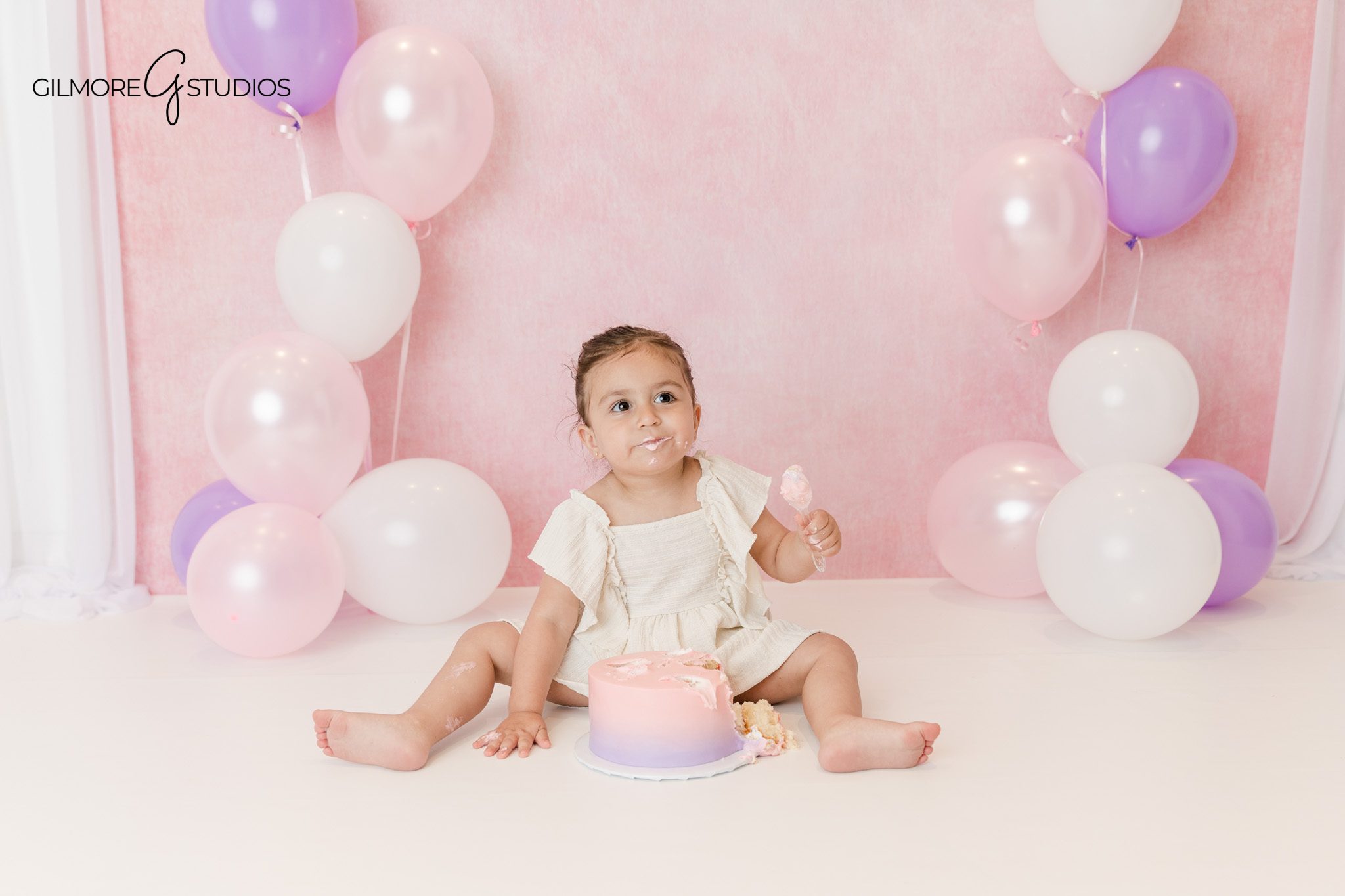 Pink and purple birthday setup for toddler and family portraits
Toddler sitting with pink and purple cake on white cake stand