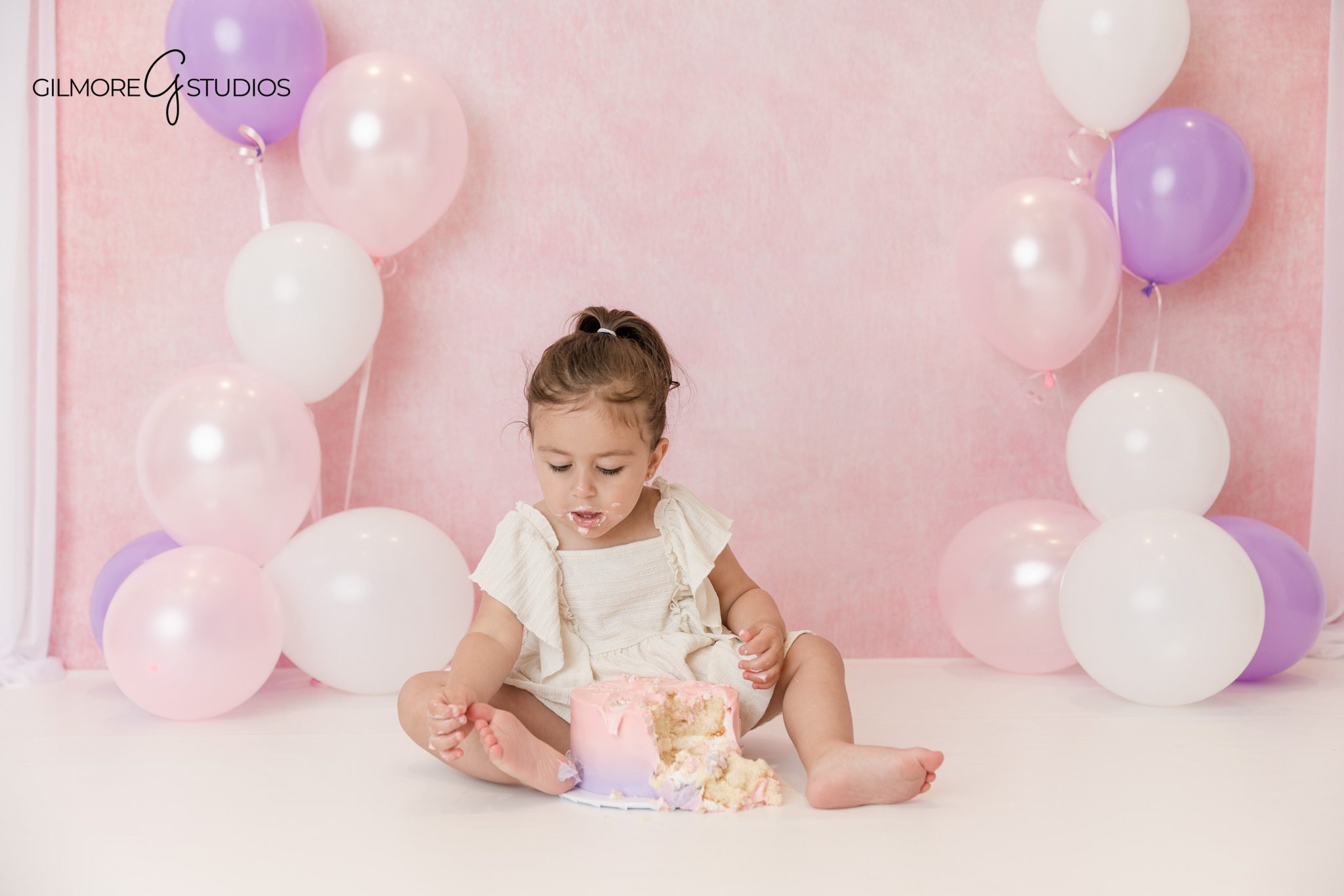 Queen Creek cake smash session with pastel balloons and white studio floor
Little girl wearing pink tulle birthday dress for studio milestone photos