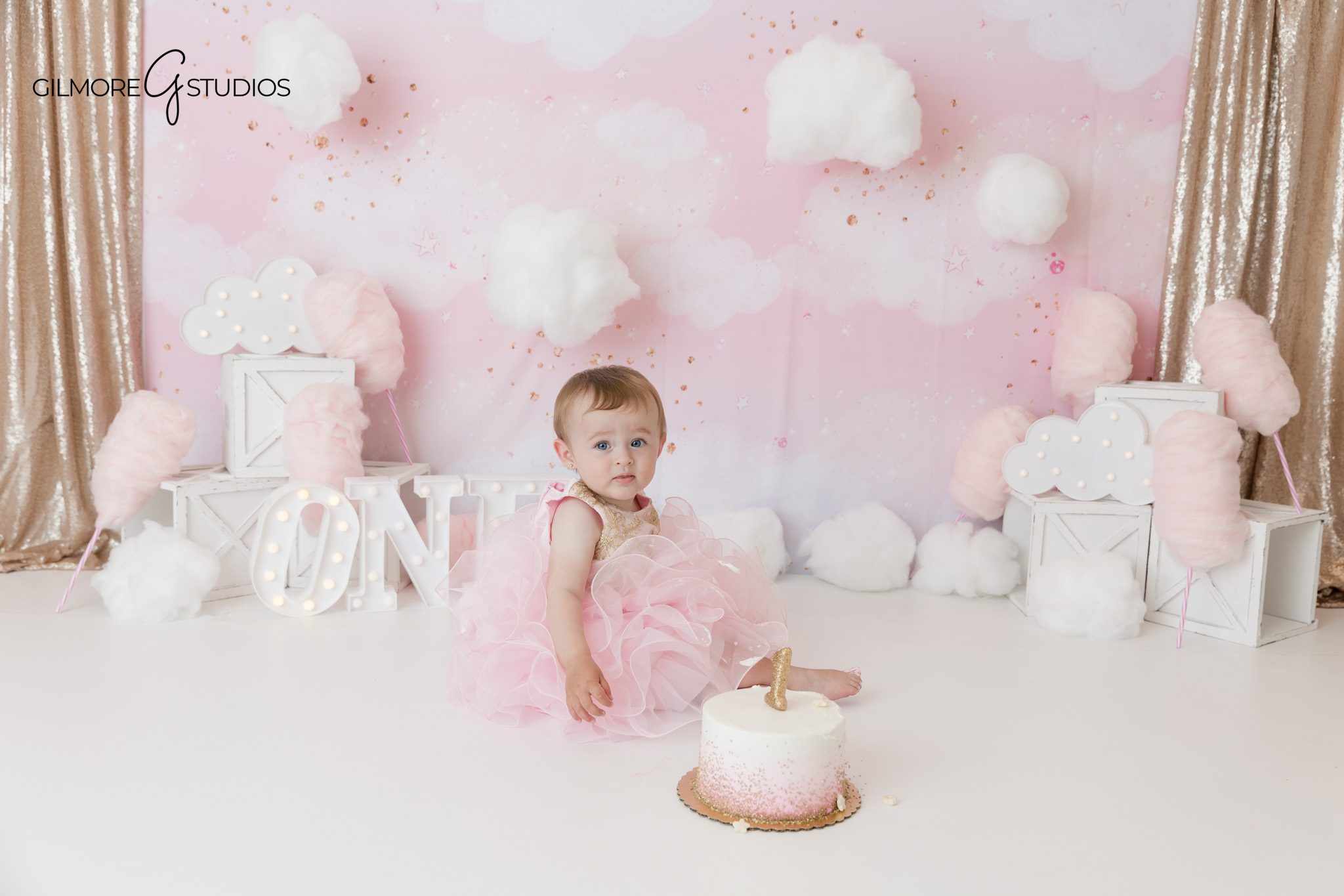 Baby girl in pink floral dress for Newport Beach cake smash photos
First birthday portrait with pink bow and floral dress on white backdrop