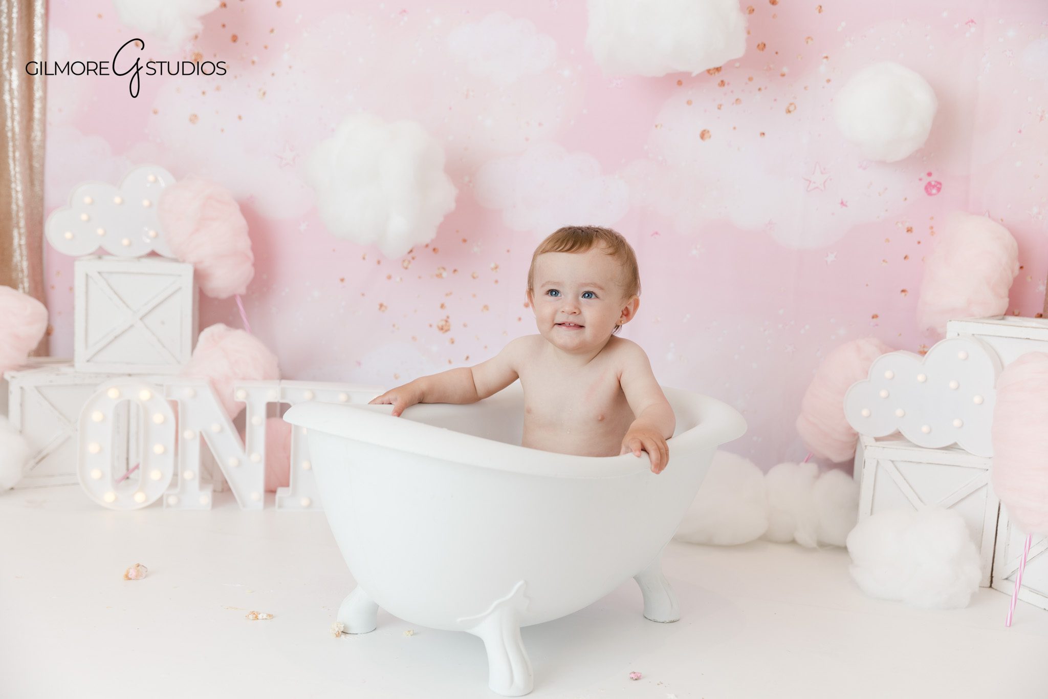 Baby girl wearing crown in pink cotton candy clouds setup
First birthday cake smash session with pink cloud backdrop