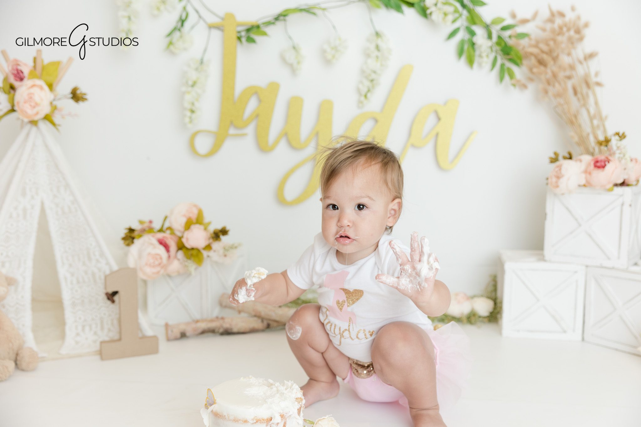 Baby girl sitting by simple white cake for first birthday photos
Floral first birthday session with soft pink and gold details