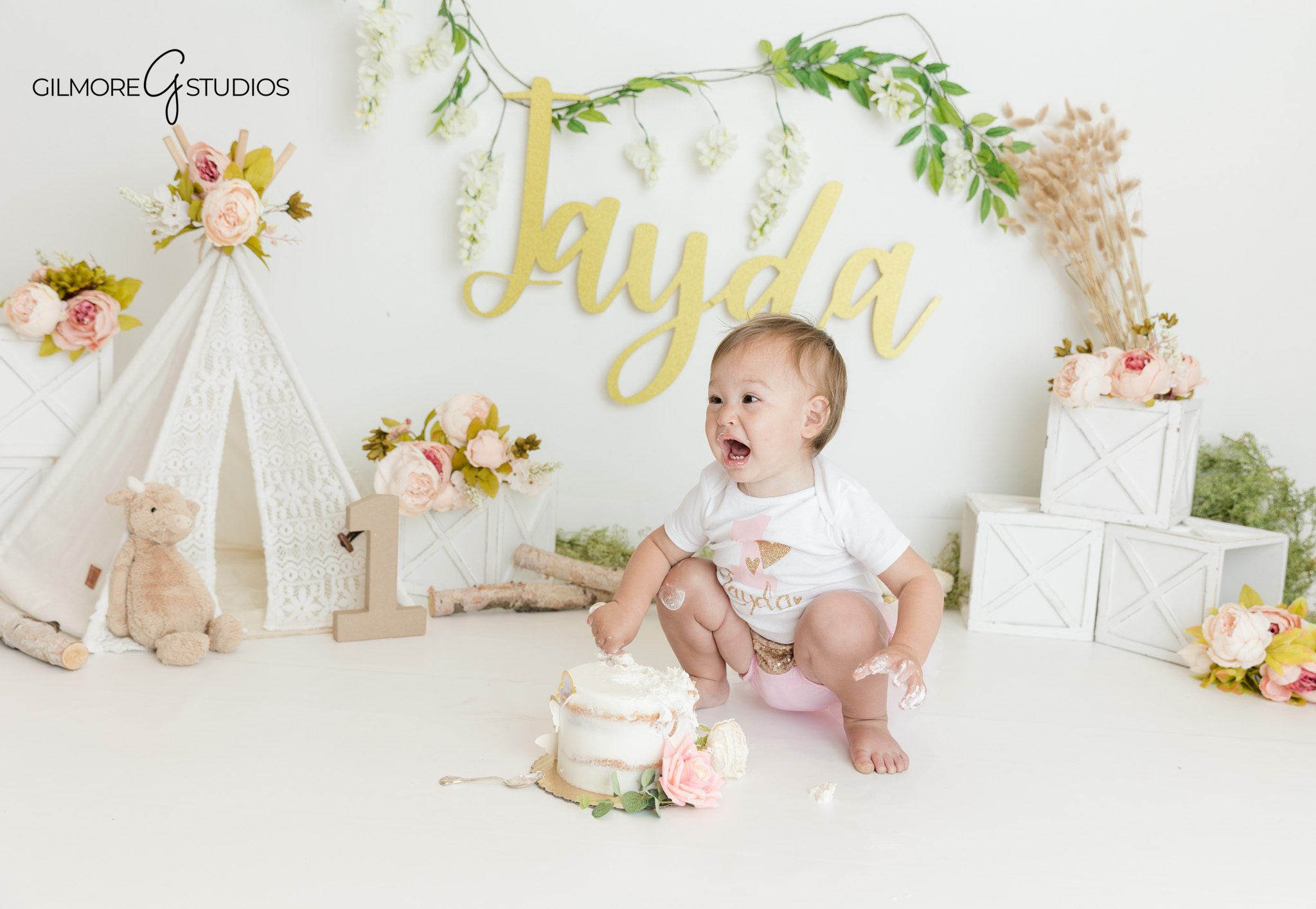 First birthday cake smash with blush flowers and greenery
Baby girl tasting cake during boho floral first birthday session