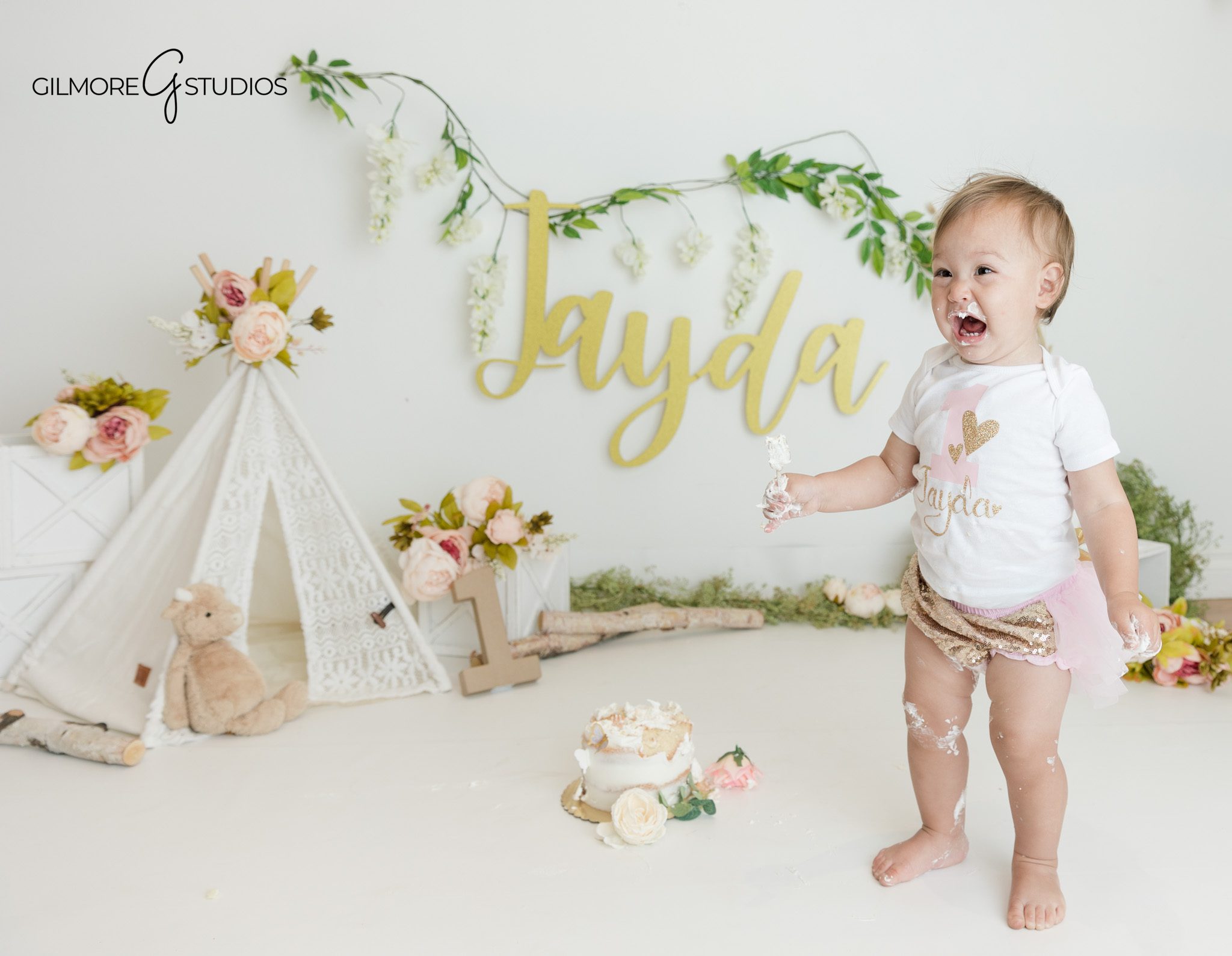 Baby girl celebrating turning one with boho floral cake smash
Soft studio first birthday setup with flowers and cake