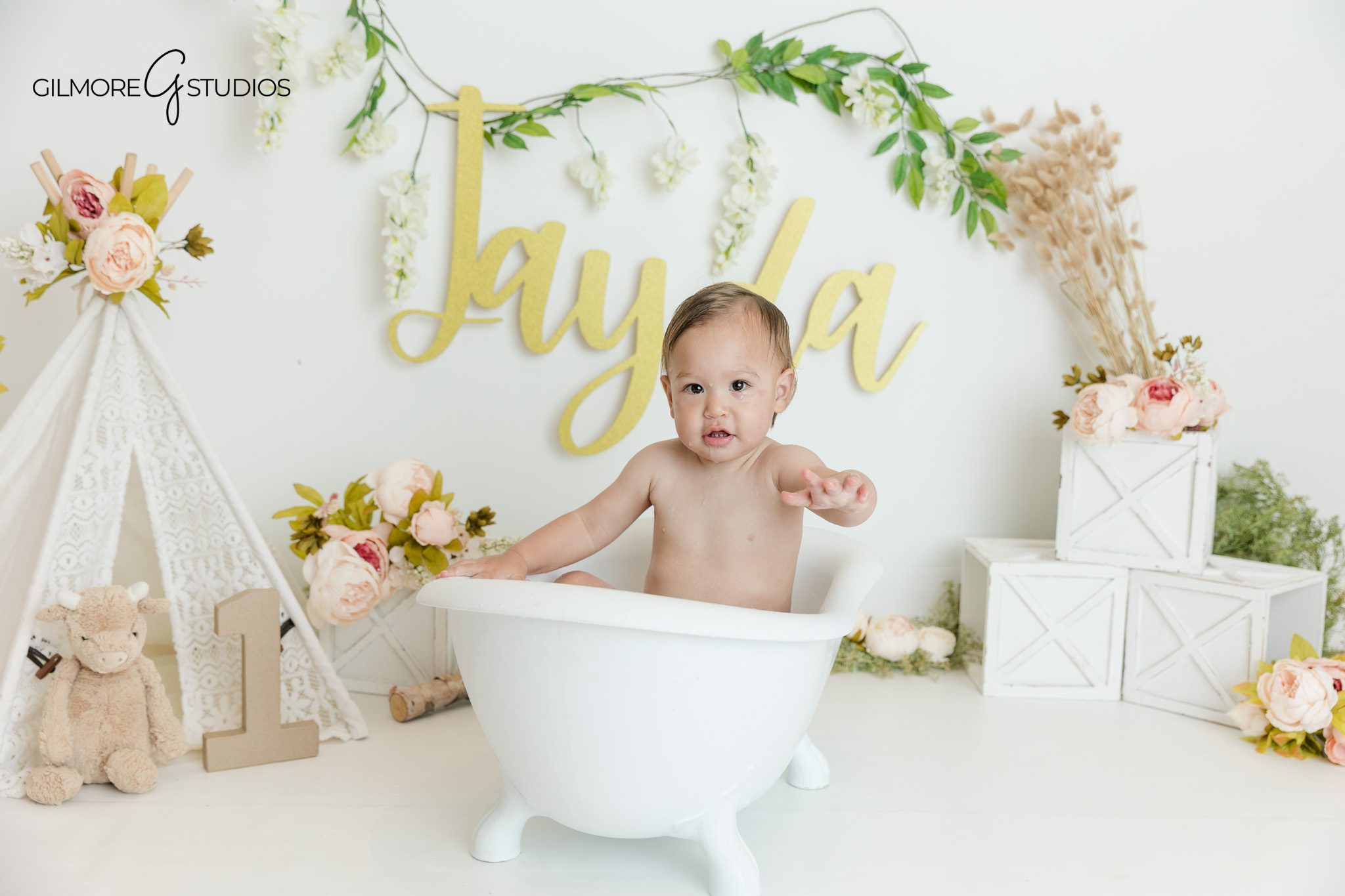Baby girl in white first birthday outfit during cake smash photos
Queen Creek cake smash session with floral teepee and neutral props