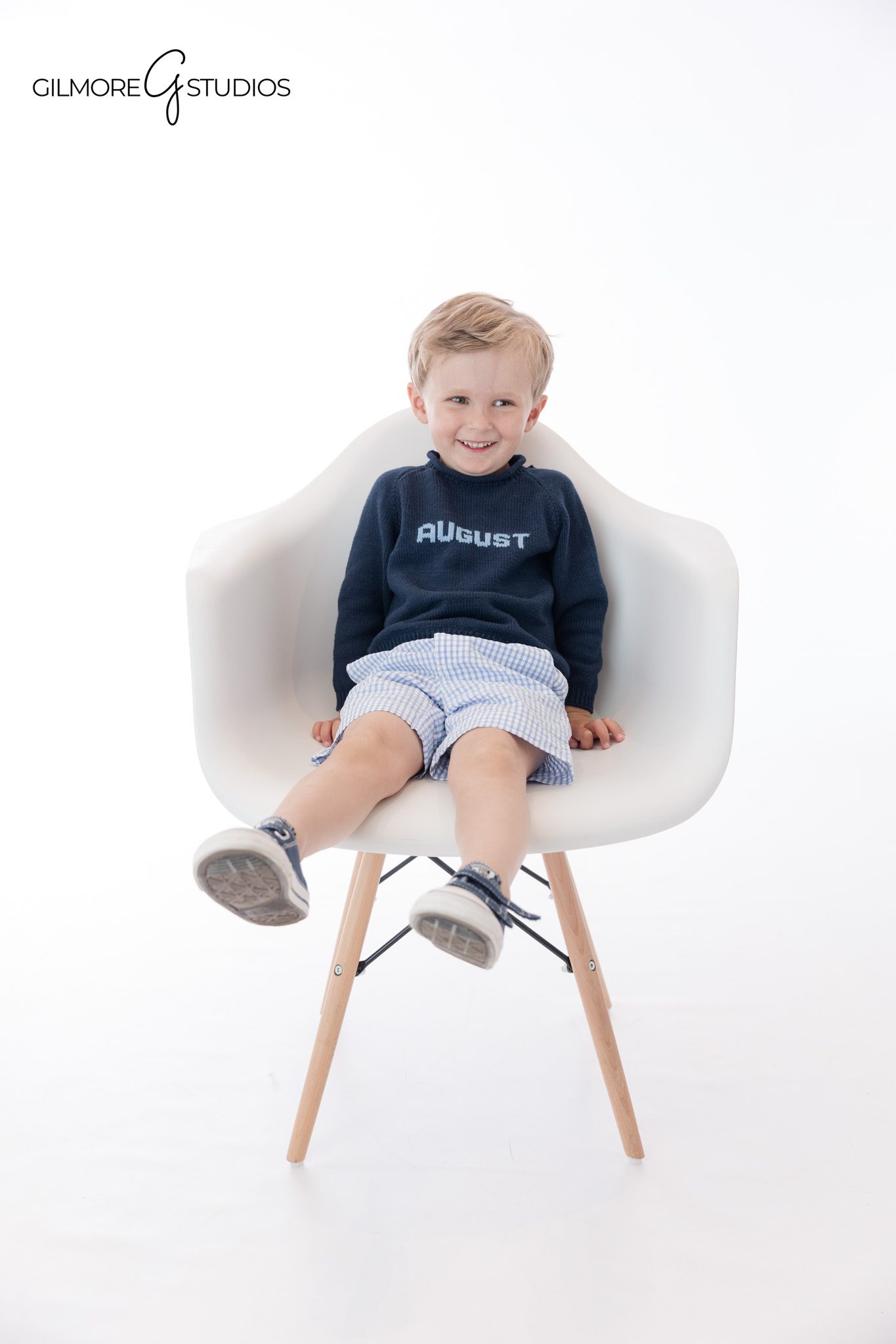 Little boy sitting in modern white chair during portrait session
Child personality portrait with classic chair pose