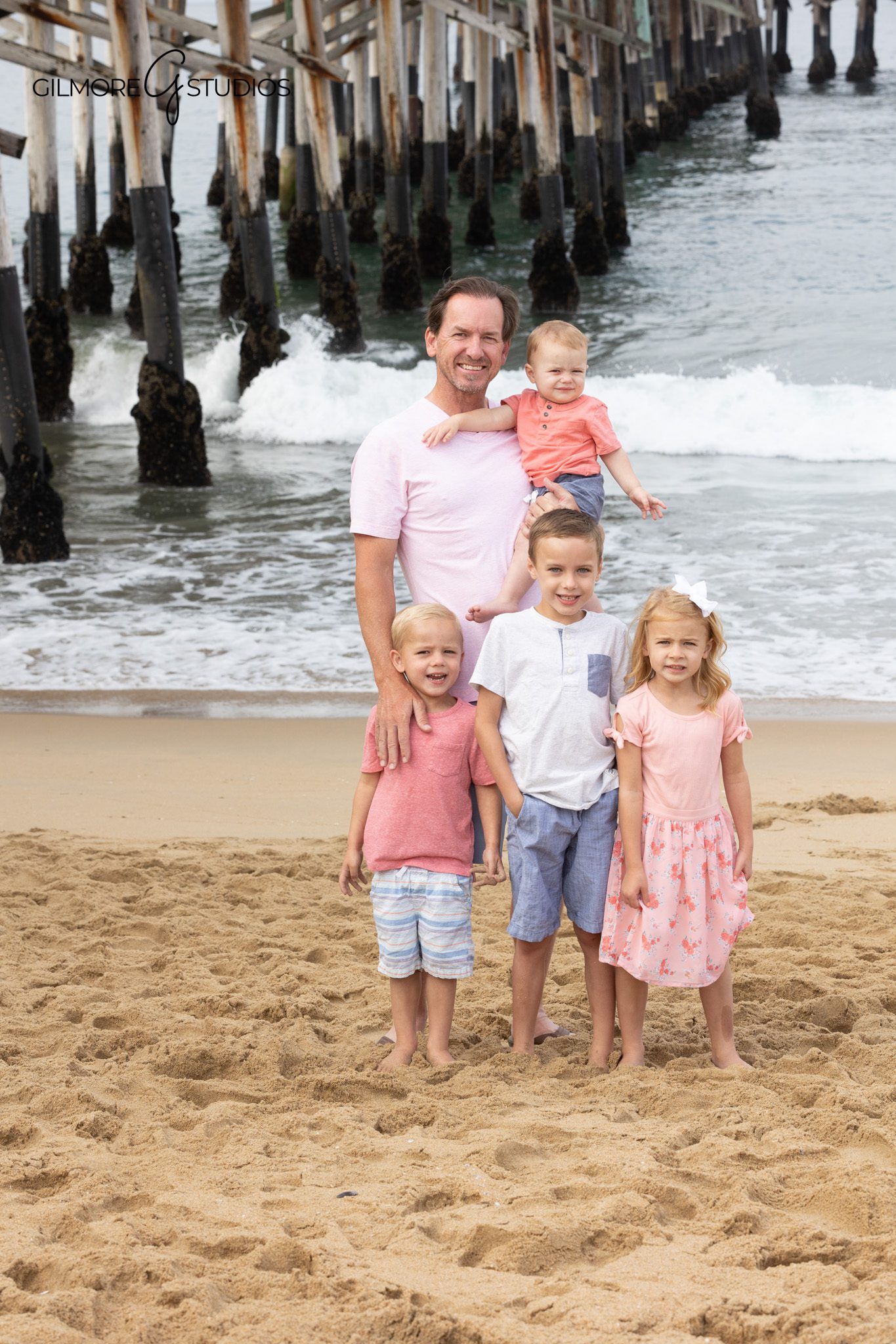 Family standing under Newport Beach Pier with waves behind them
Newport Beach Pier portraits for a family with young kids
