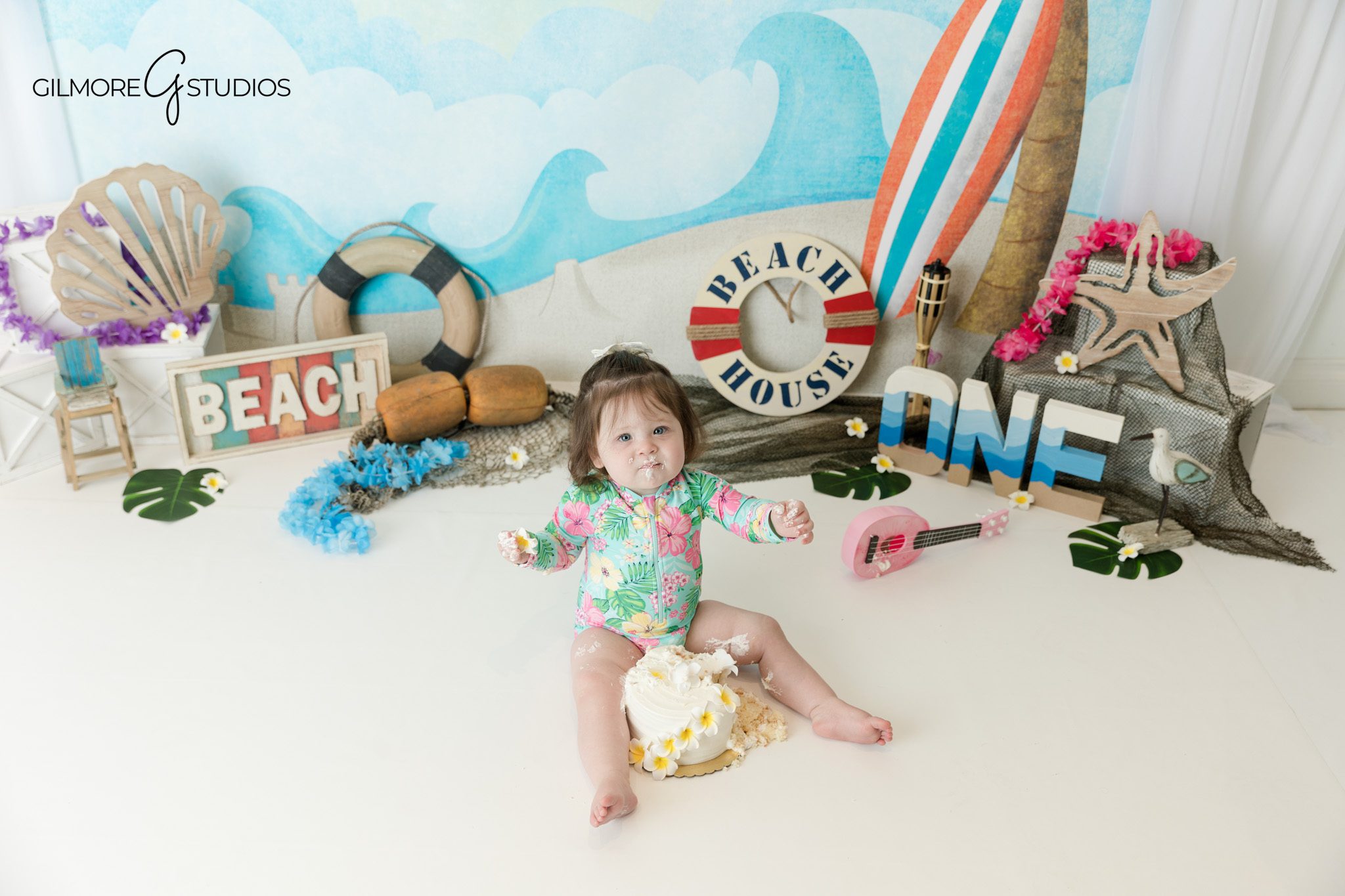 Beach themed cake smash setup with tropical props and white cake
First birthday cake with white flowers for beach themed session