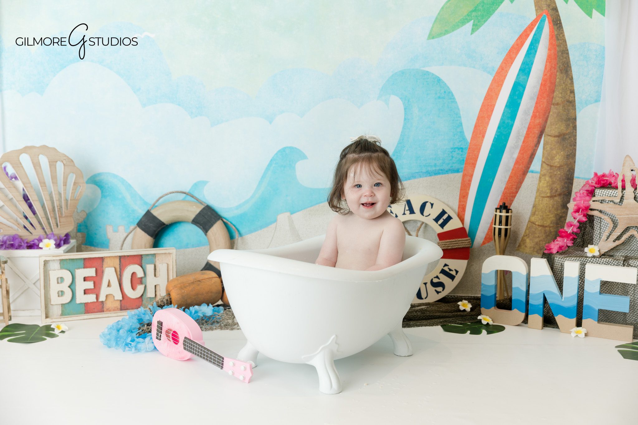 Beach theme cake smash with blue ocean backdrop and palm tree
One year old baby girl with cake and beach props
